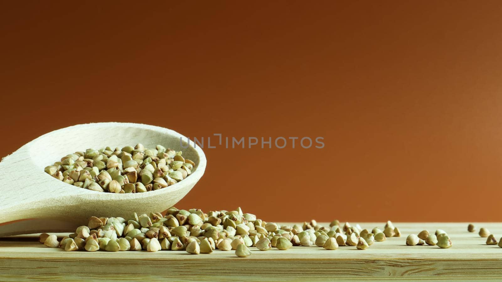 Green buckwheat in a wooden spoon on a brown background. Great food. healthy groats. Organic raw non-fried vegetarian food. The concept of a healthy and balanced diet. Dietary foods. Copy space.