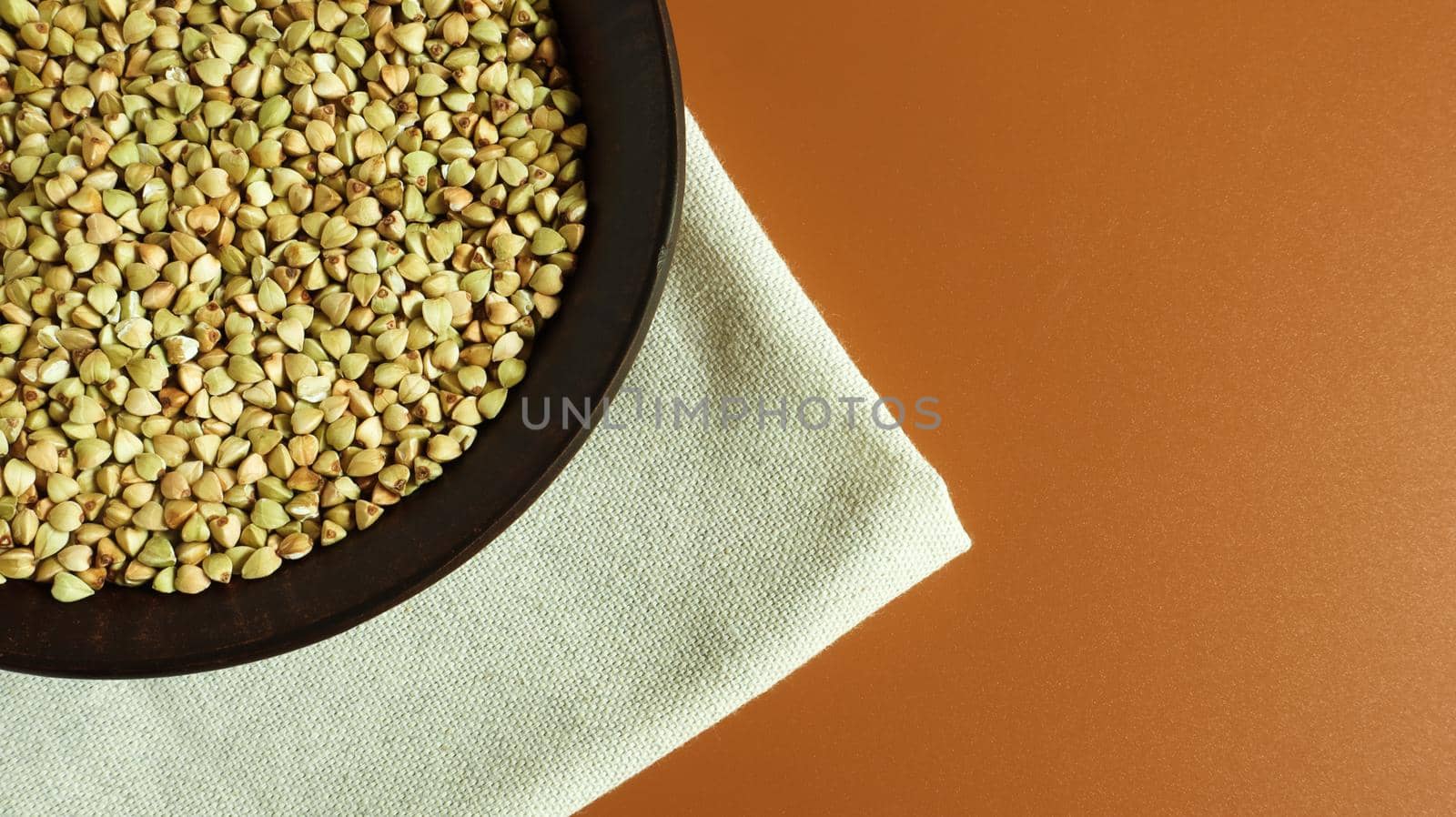 Raw green buckwheat in a brown clay plate on a brown background. Vegan organic food concept. The concept of diet, weight loss, healthy and proper nutrition. Copy space for text. Top view, flat lay.