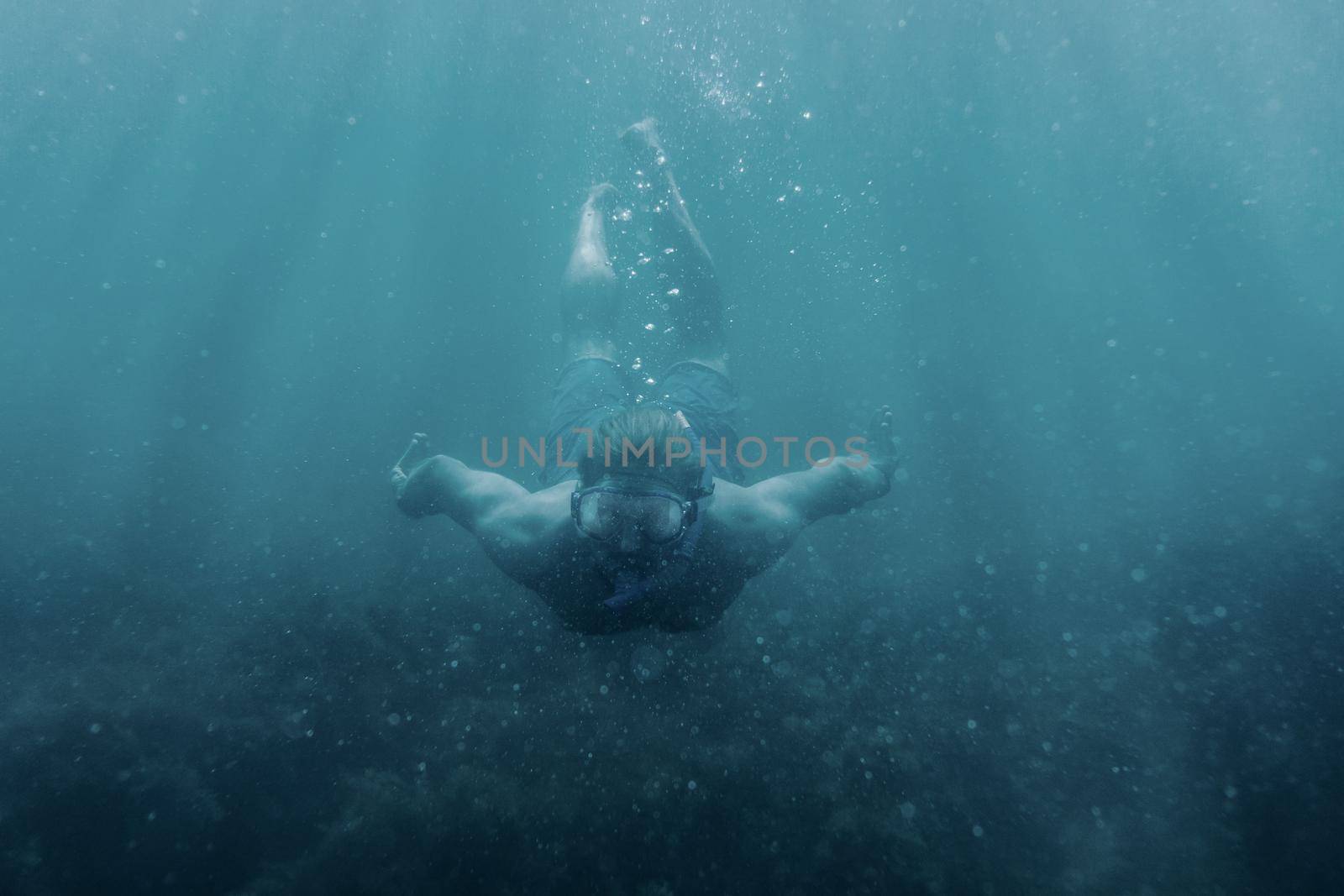 Active male freediver in mask swimming underwater, front view.