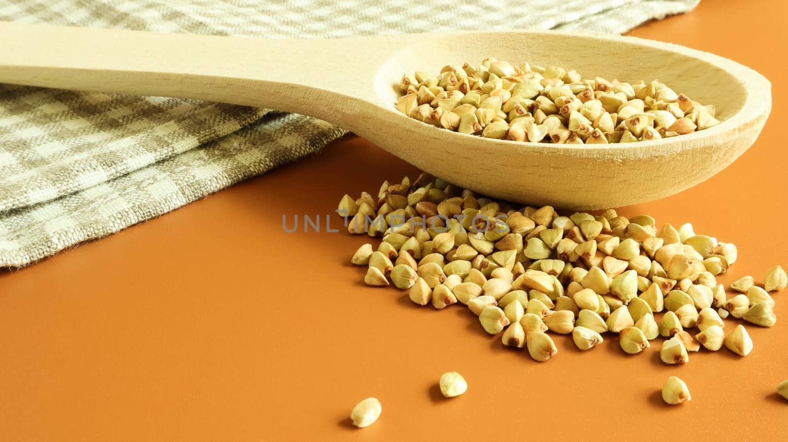 Green buckwheat in a wooden spoon on a brown background. Great food. healthy groats. Organic raw non-fried vegetarian food. The concept of a healthy and balanced diet. Dietary foods. Copy space.