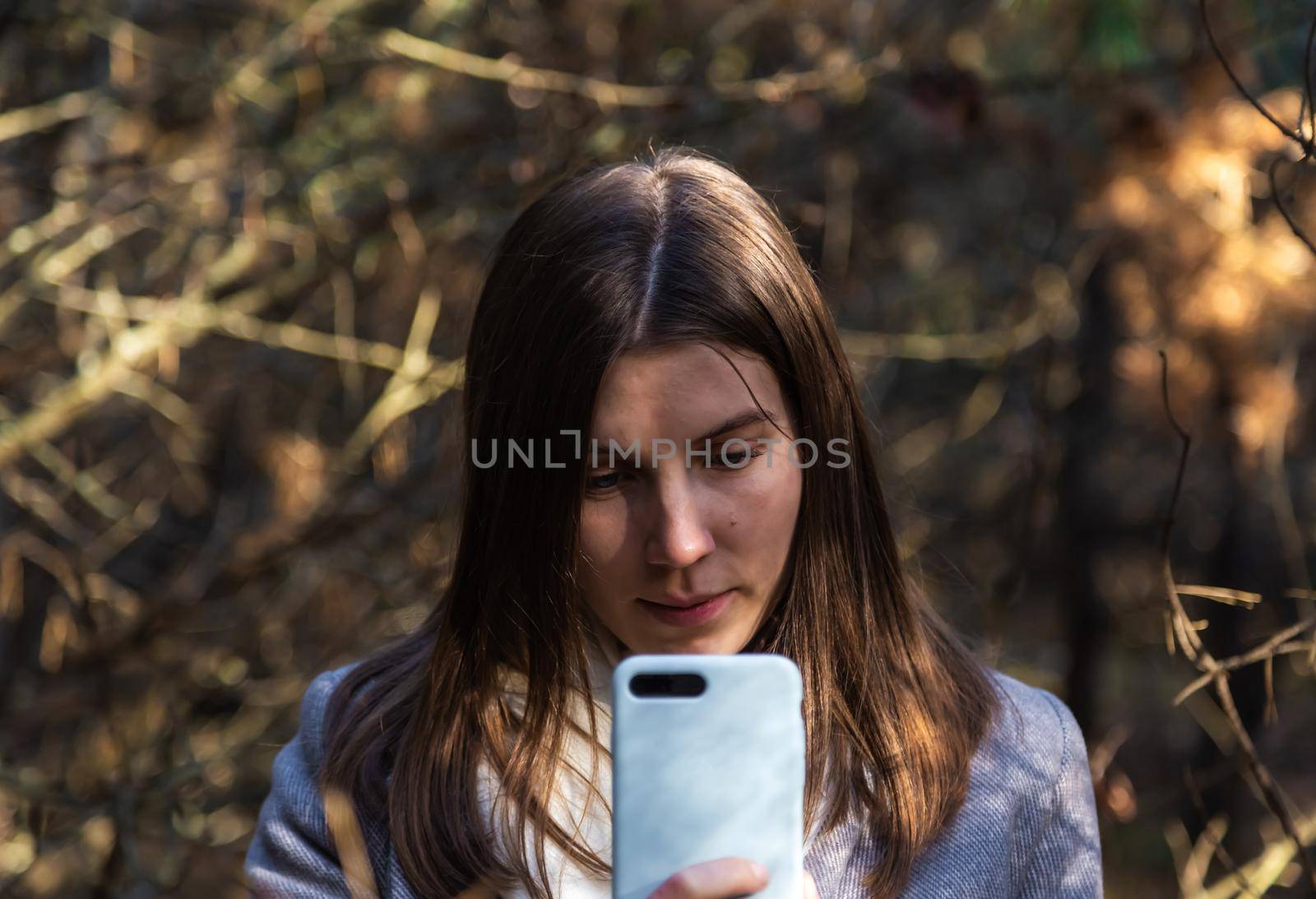 Girl in a gray coat takes a selfie in the forest. Outdoor communication mobile phone.