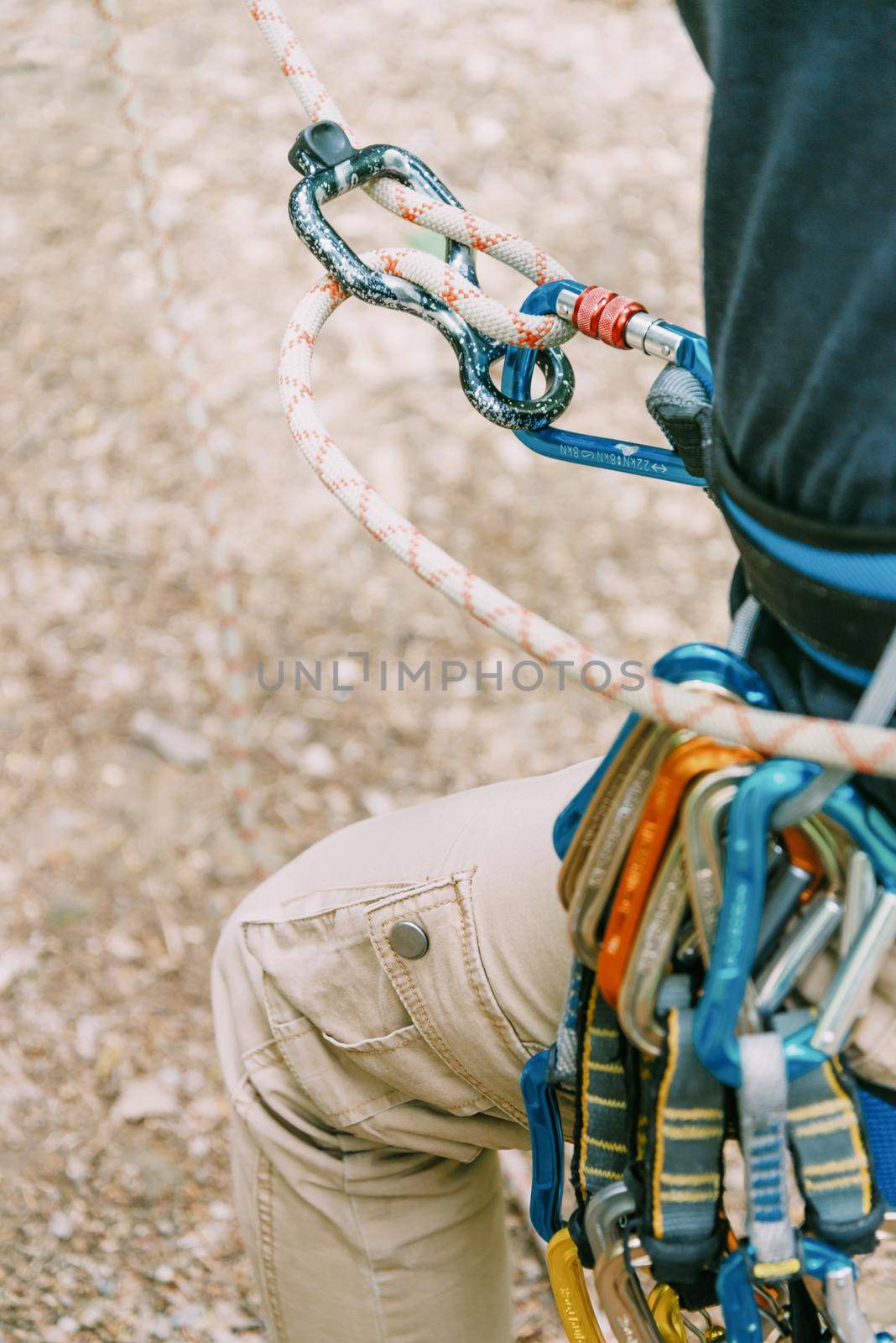 Unrecognizable climber in safety harness belaying with rope, close-up.