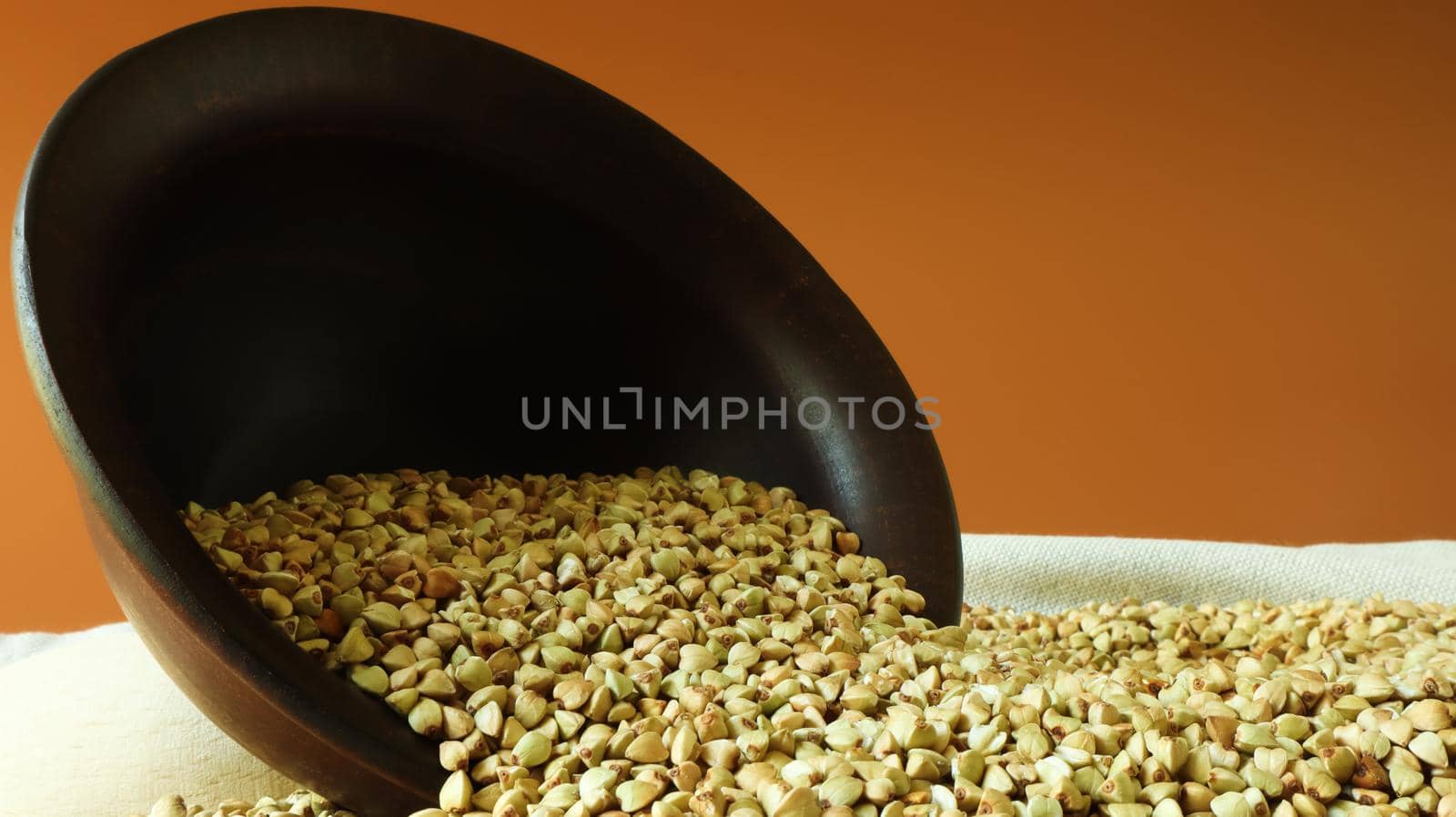 Buckwheat scattered background, raw green buckwheat in a brown clay bowl or plate. Healthy groats. Organic raw non-fried vegetarian food. The concept of a healthy and balanced diet. Diet food.