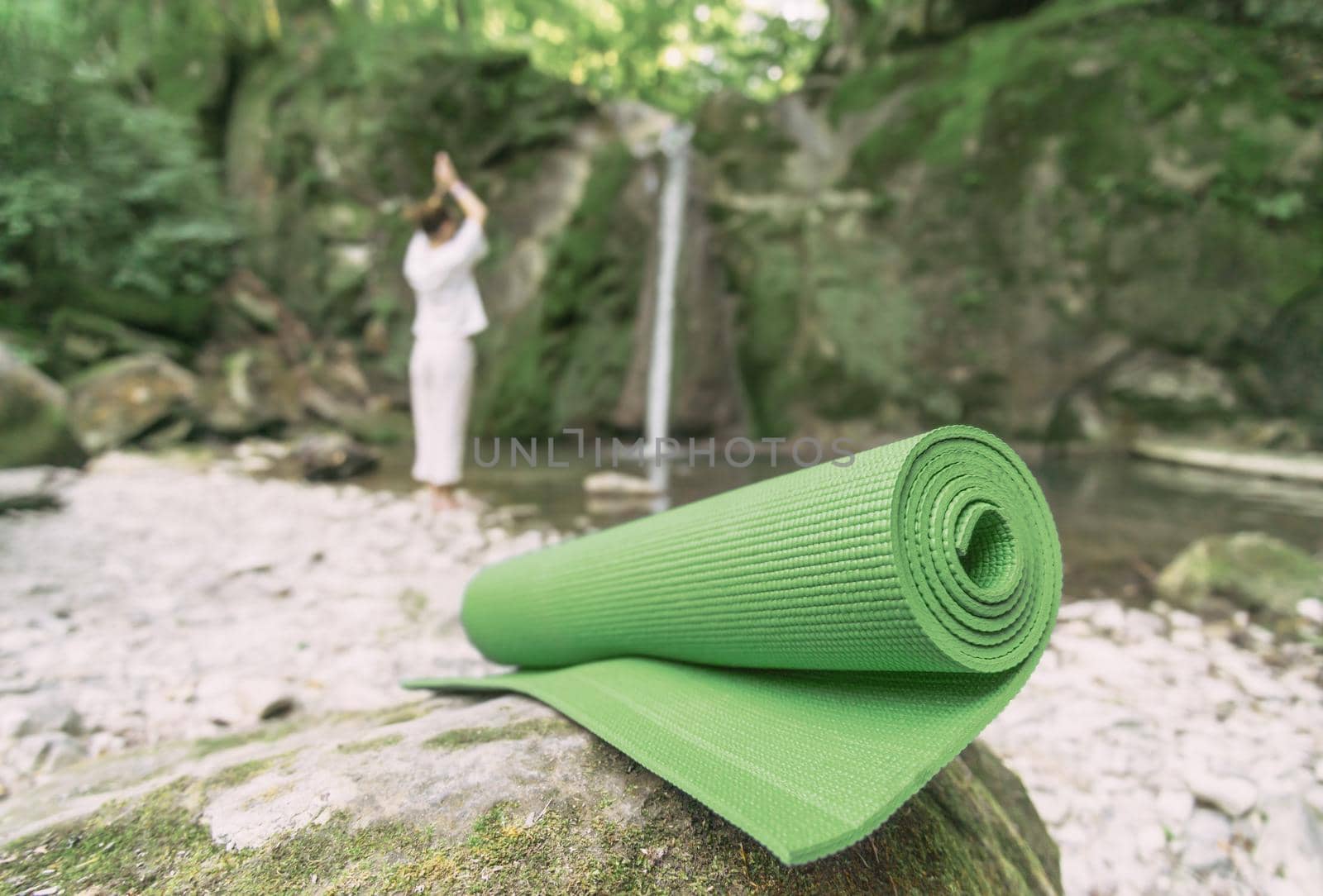 Yoga mat in front of silhouette of young woman exercising and meditating outdoor.