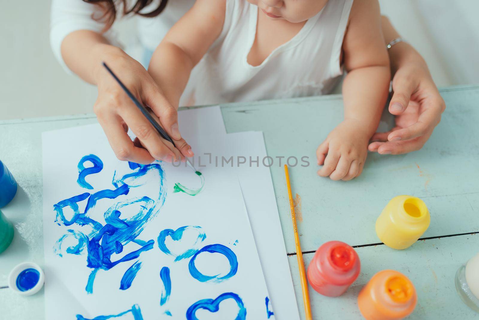 Mother and daughter painting together at home with paintbrushes and watercolors by makidotvn