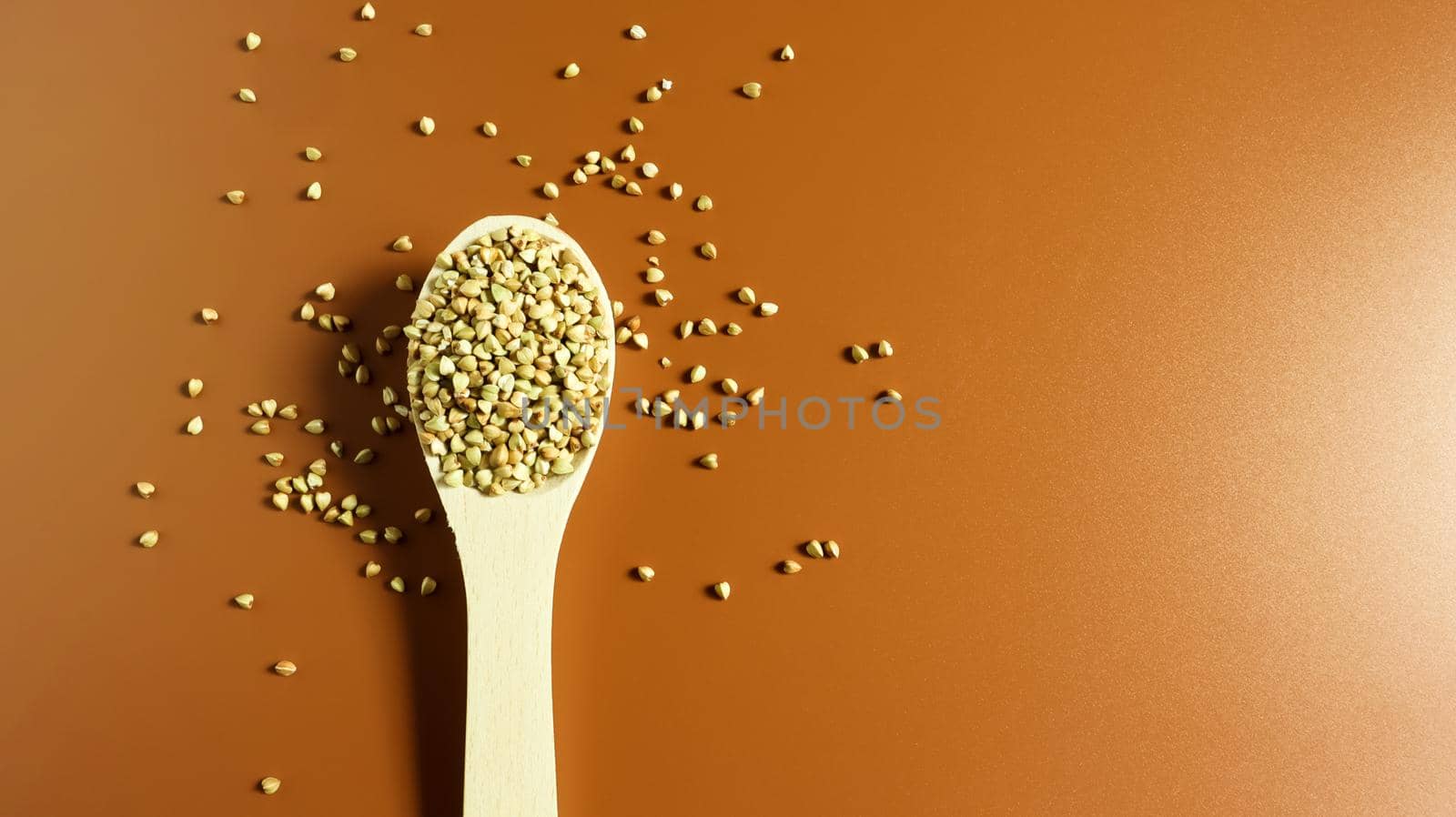 Green buckwheat in a wooden spoon on a brown background. Great food. healthy groats. Organic raw non-fried vegetarian food. The concept of a healthy and balanced diet. Dietary foods. Copy space.