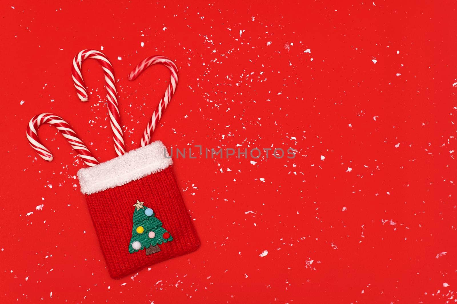 Red knitted Christmas bag with Christmas striped candy at red snowy background, copy space, Christmas and new year concept.