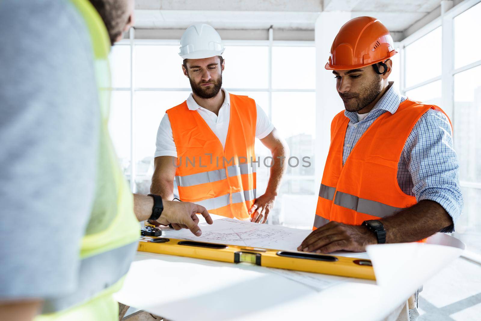 Two engineers man looking at project plan on the table in construction site by Fabrikasimf