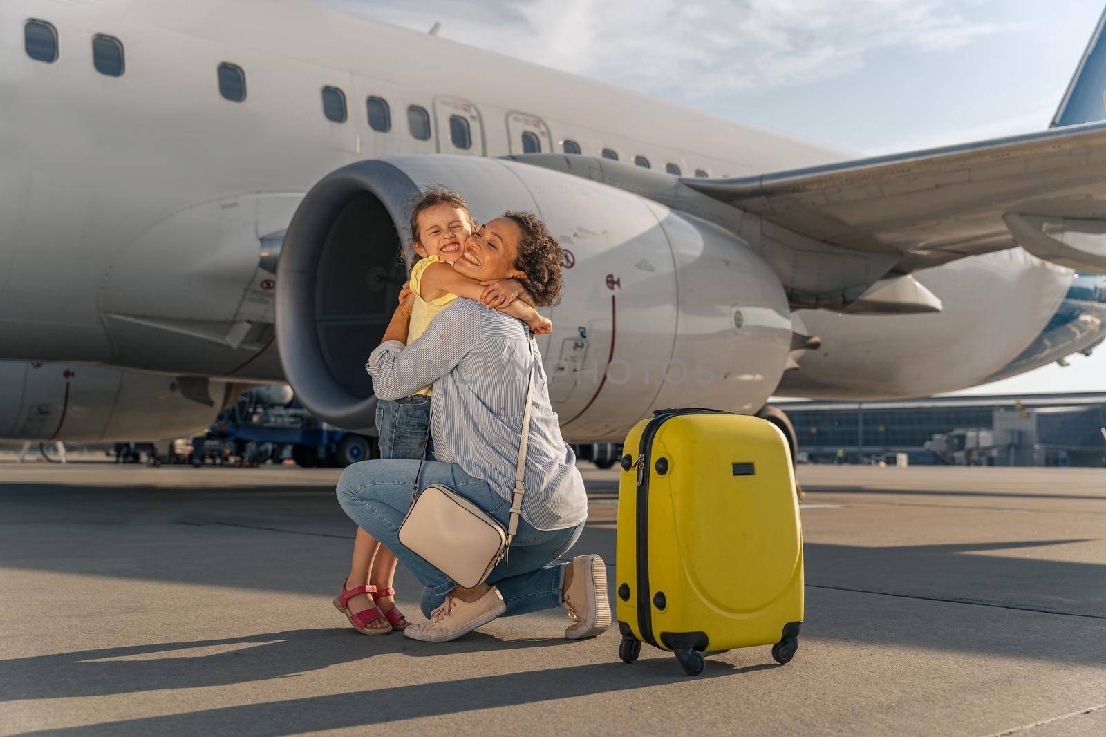 Smiling adult lady hugging her child near the plane outdoor by Yaroslav_astakhov