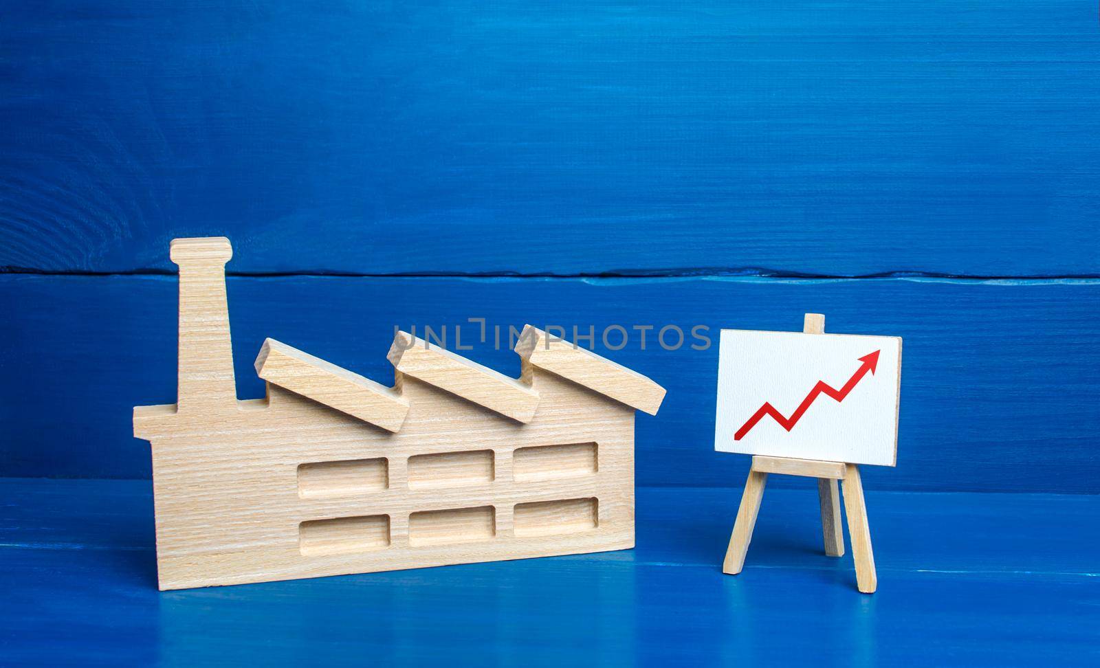 Figurine of industrial factory plant and easel with a red up arrow chart. Increased production volumes, high income, energy resource consumption, emissions and pollution. Industry and economy growth.