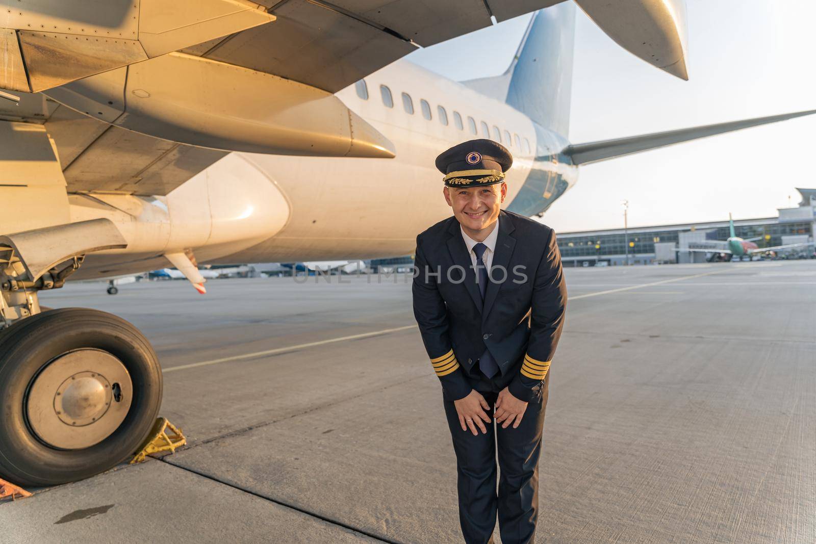 Smiling adult pilot in black suit standing near big white plane outdoor