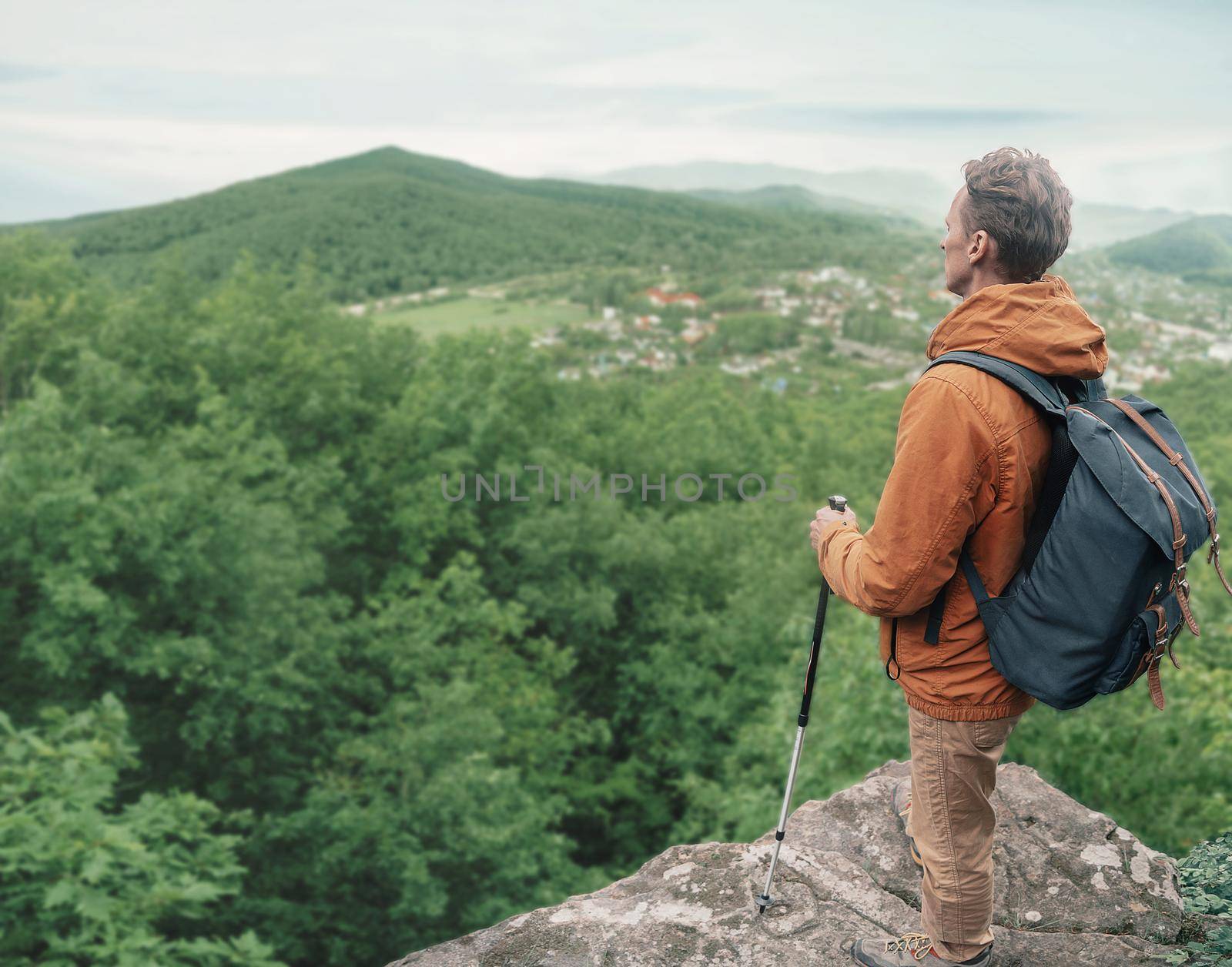 Explorer backpacker young man with trekking poles standing on edge of cliff and looking into the distance outdoor.