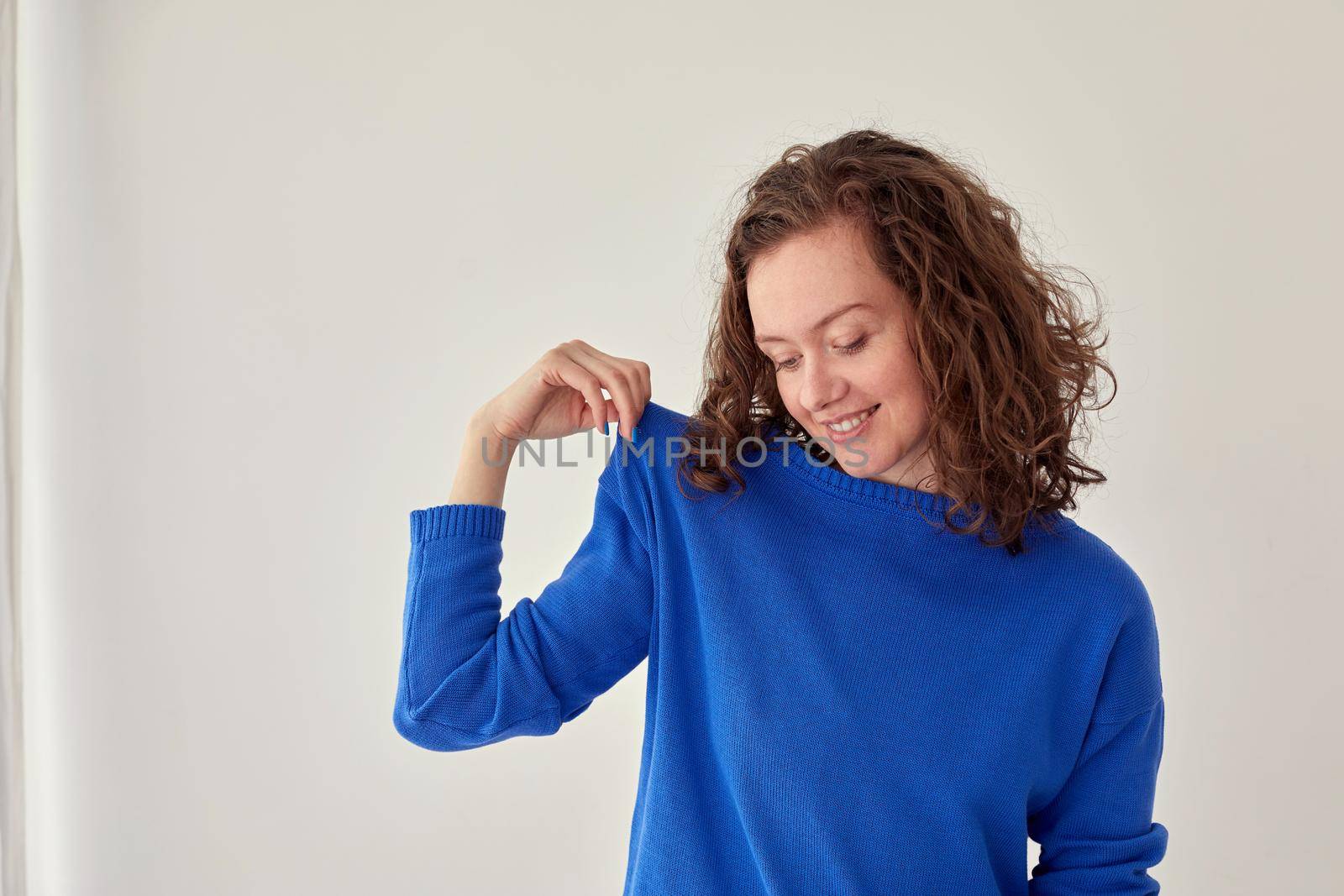 Young female model in trendy oversize blue woolen sweatshirt looking at camera against white background