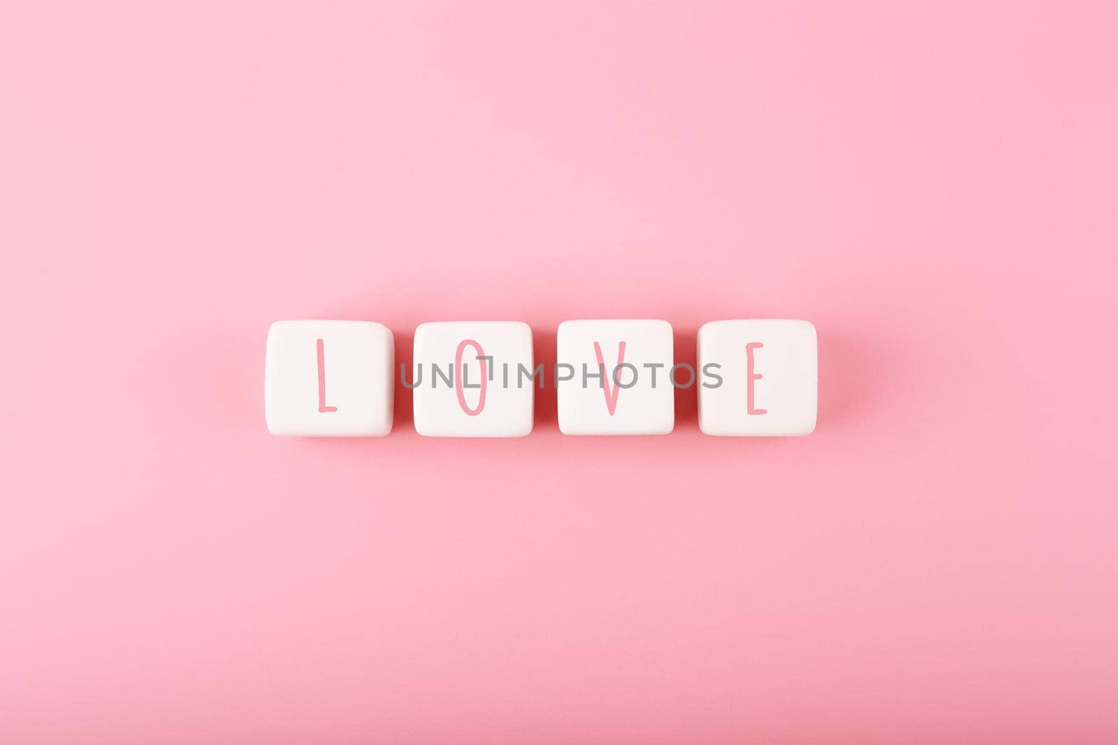 Word love written on white toy cubes against pink background with copy space. Minimal trendy concept of Valentine's day, love emotions, anniversary or dating