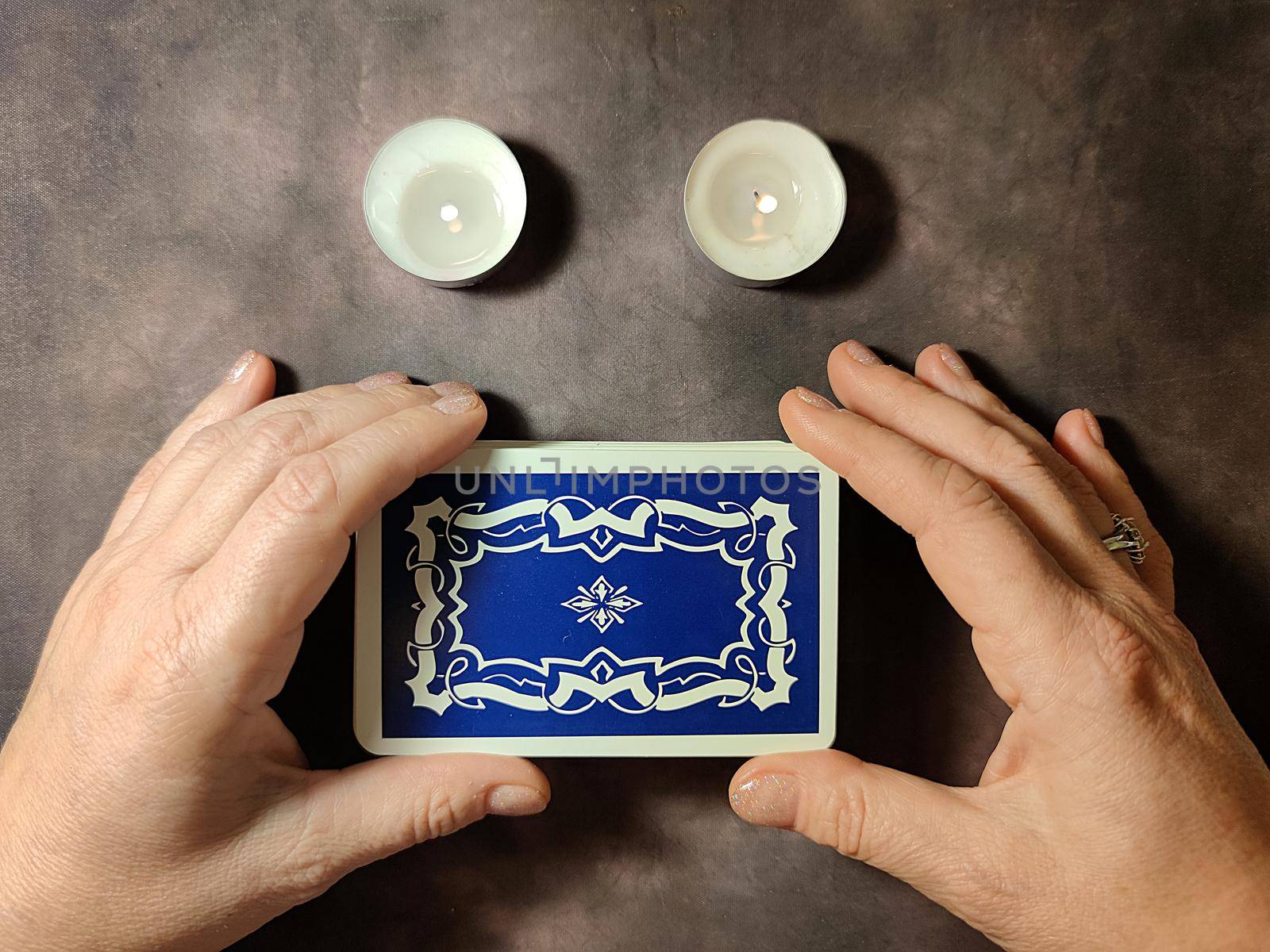 deck of tarot cards in female hands and candles on dark vintage background.