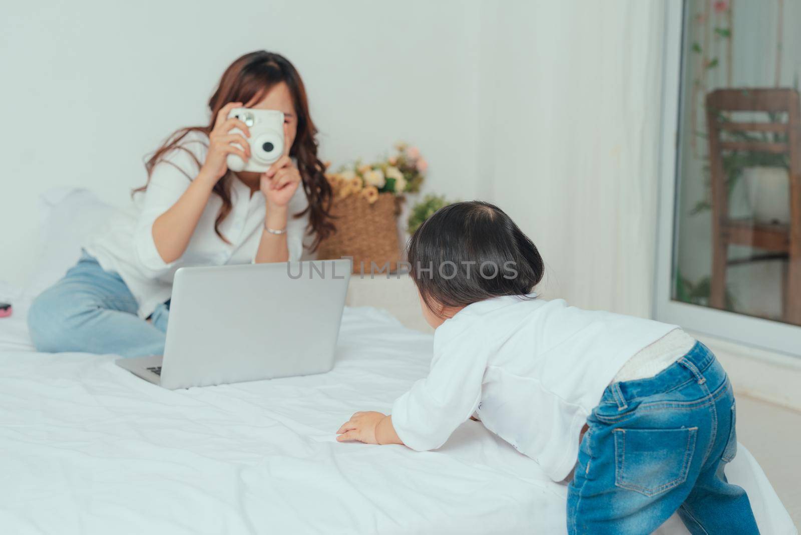 Image of young cheerful asian mother taking photo her baby on camera in cozy room