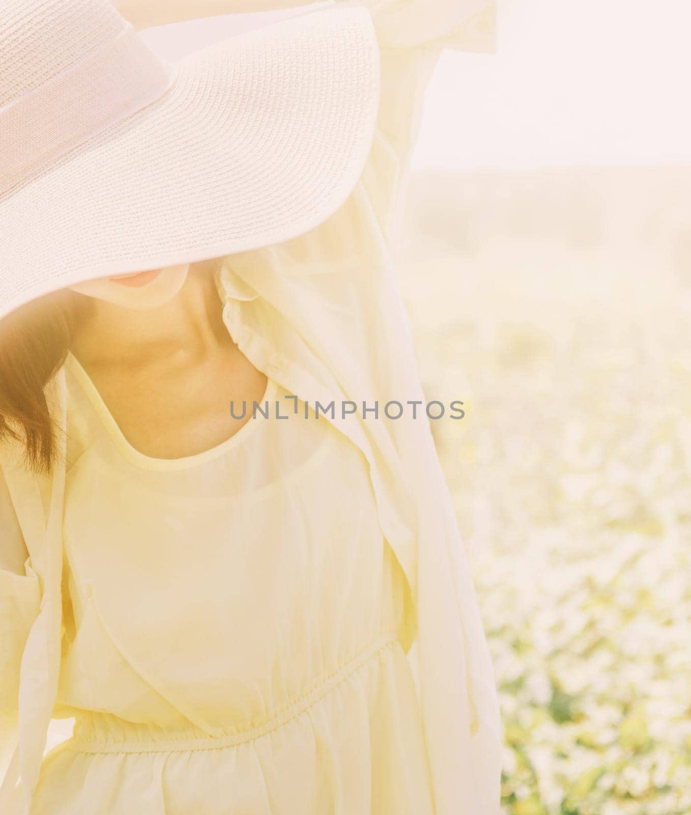 Beautiful young woman in hat with wide brim and yellow dress walking on summer sunny day.