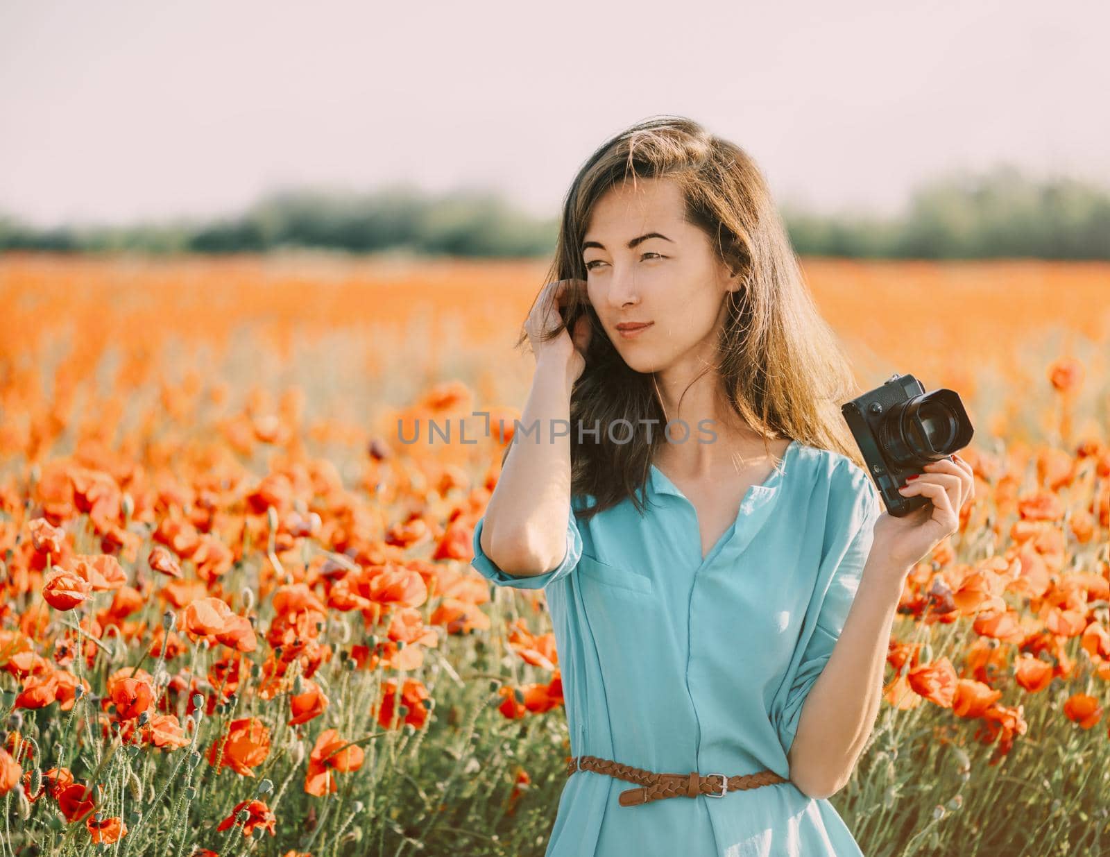 Photographer beautiful brunette young woman in blue dress standing in poppy meadow.