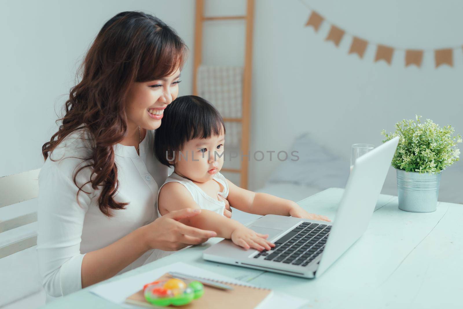 Working mother concept. Young woman working on laptop with her child from home by makidotvn