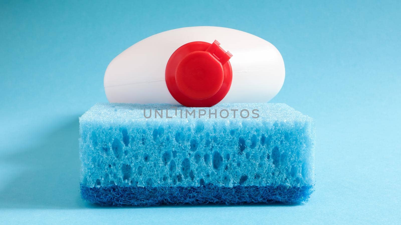One blue sponge with a white bottle of detergent on a blue background. Convenience of sponges consists in good detergent retention that allows to use it economically.