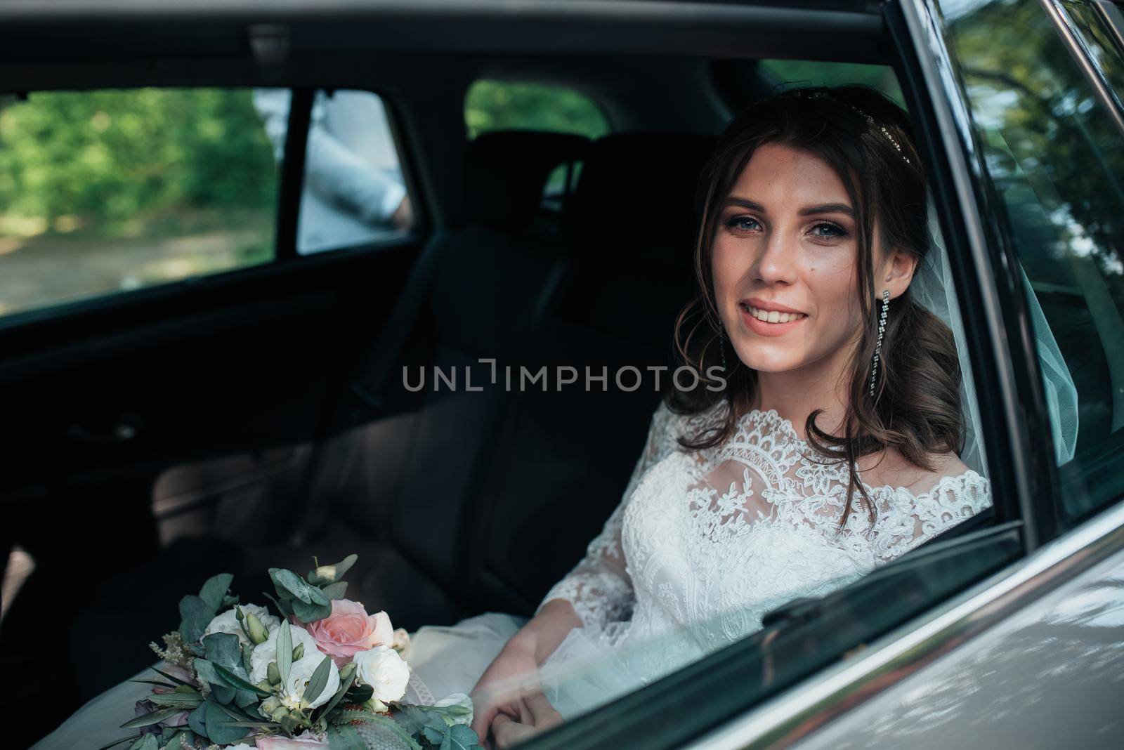 Wedding photo of the bride who is sitting in the car with a bouquet of flowers
