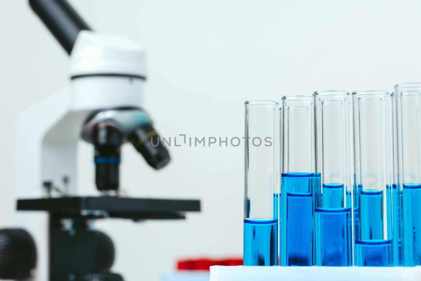 Microscope and colored test tubes on table in laboratory, close up