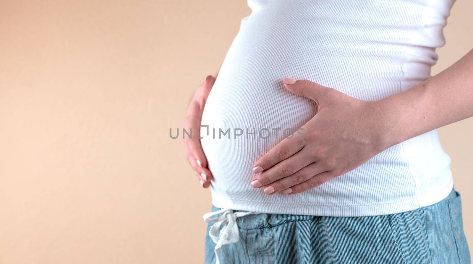 Authentic close up shot of an young pregnant woman in pajamas is caressing her belly just woke up in a bedroom in the morning