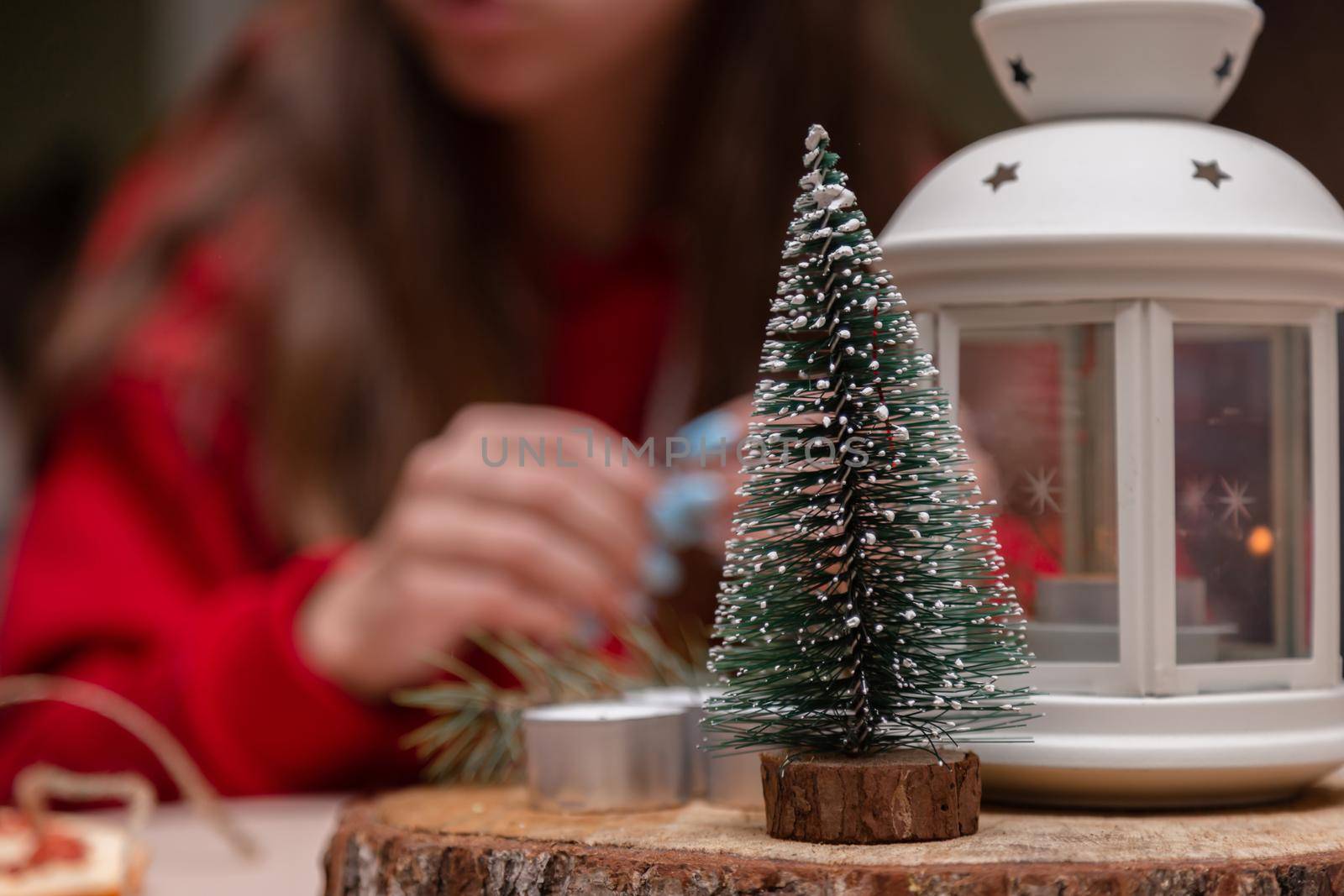 Decorative Christmas tree toy standing on a wooden stand. girl sitting at the table. blurred background.