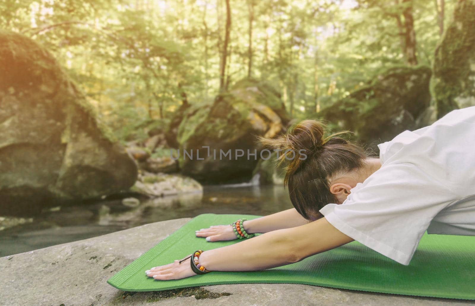 Young woman is stretching on yoga mat in forest outdoor.