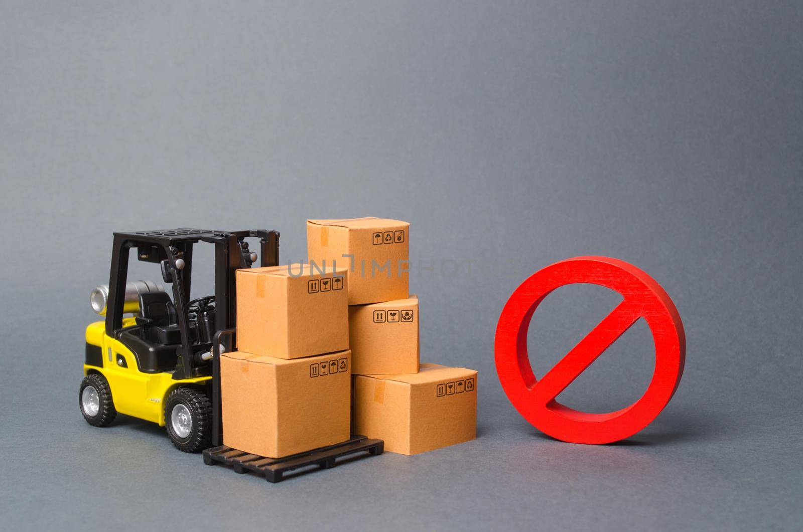 Forklift truck near cardboard boxes and a red symbol NO. Embargo, trade wars. Restriction on the importation of goods, proprietary for business. Inability to sell products, ban import. No delivery.