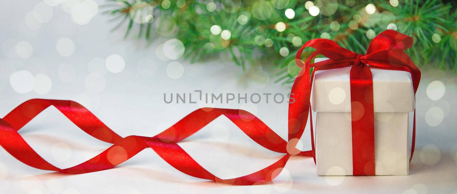 Christmas Holiday Composition. New Year Gift in White Box with Red Ribbon on Light Background with Fir Tree. Copy Space For Your Text