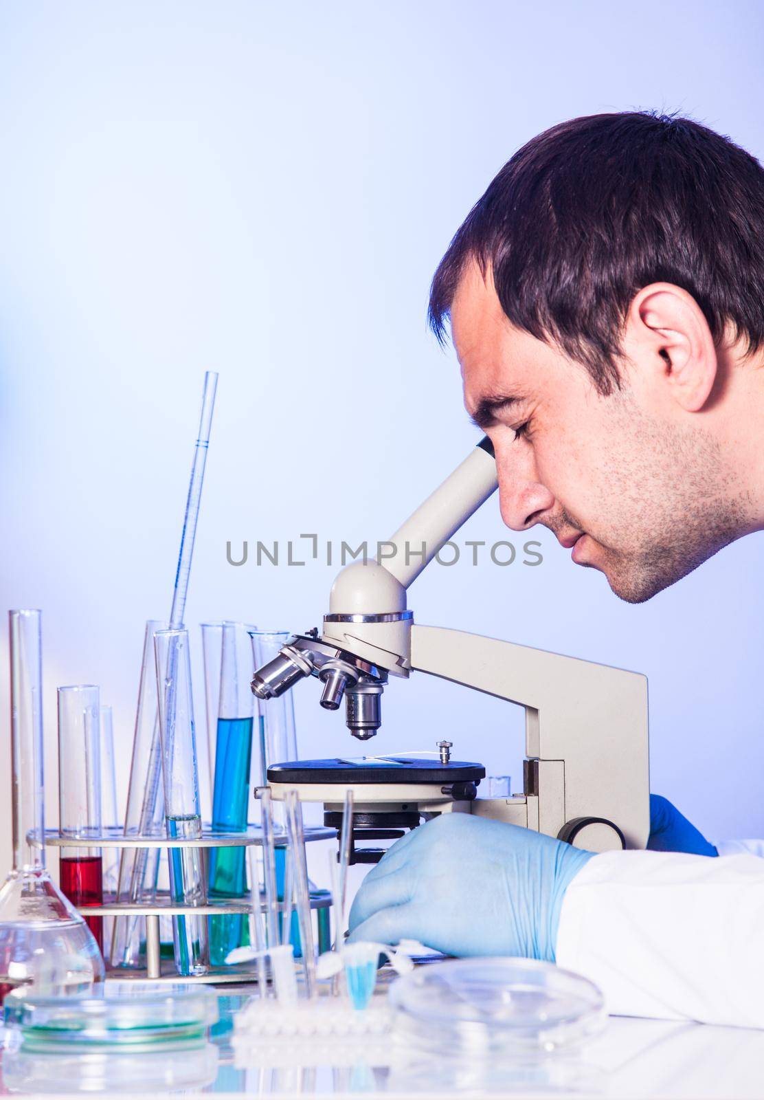 Man is looking into the ocular of microscope, doing reseach