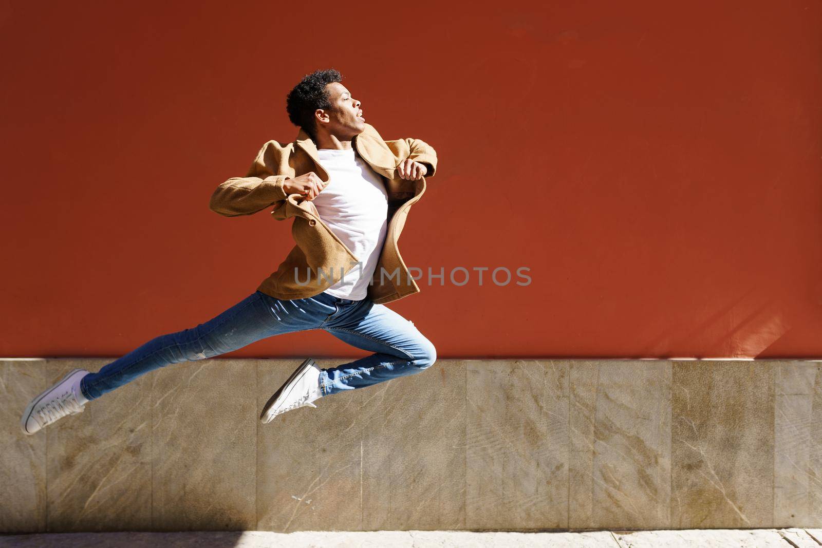 Young black man doing an acrobatic jump on red urban wall. Cuban guy.