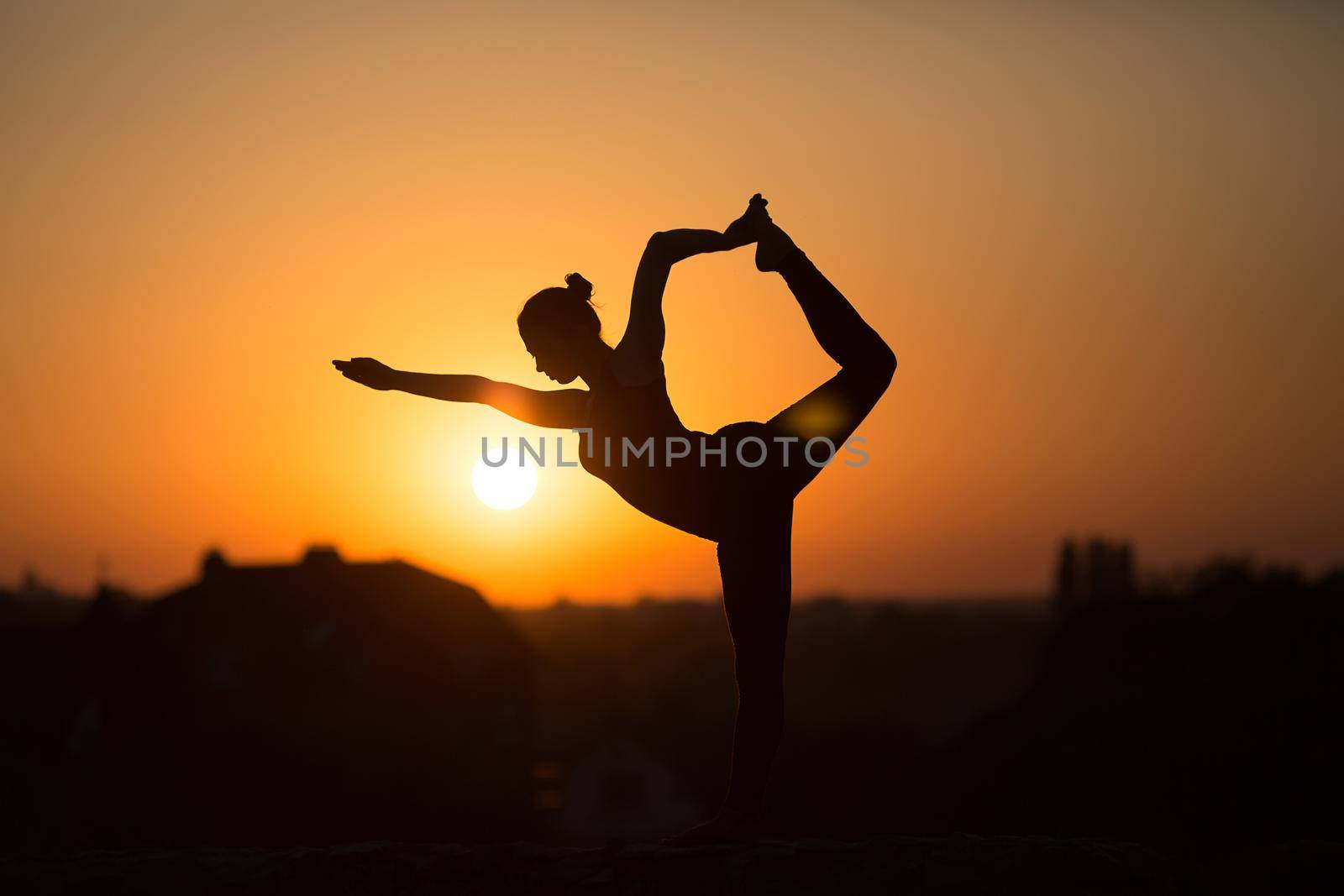 Silhouette of woman doing yoga over orange sun