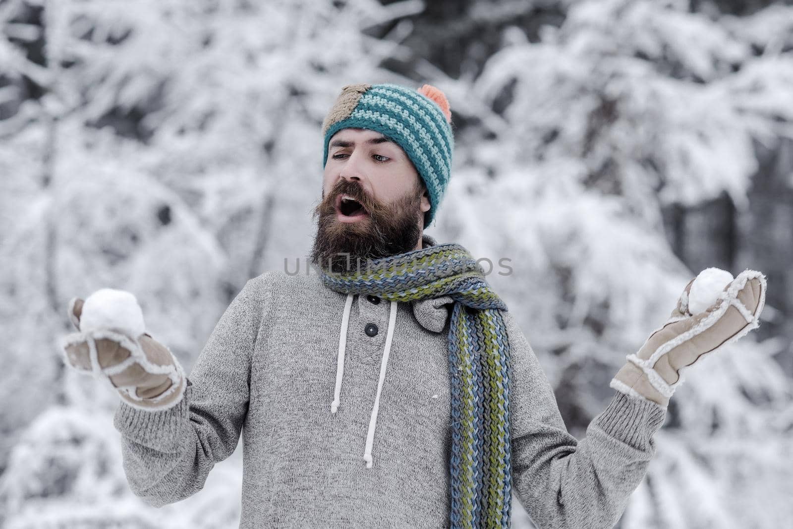 Bearded man with snowballs in snowy forest. Skincare, beard care in winter. Hipster in jacket, hat, scarf, beard warm in winter. Snow fight, winter rest by Tverdokhlib