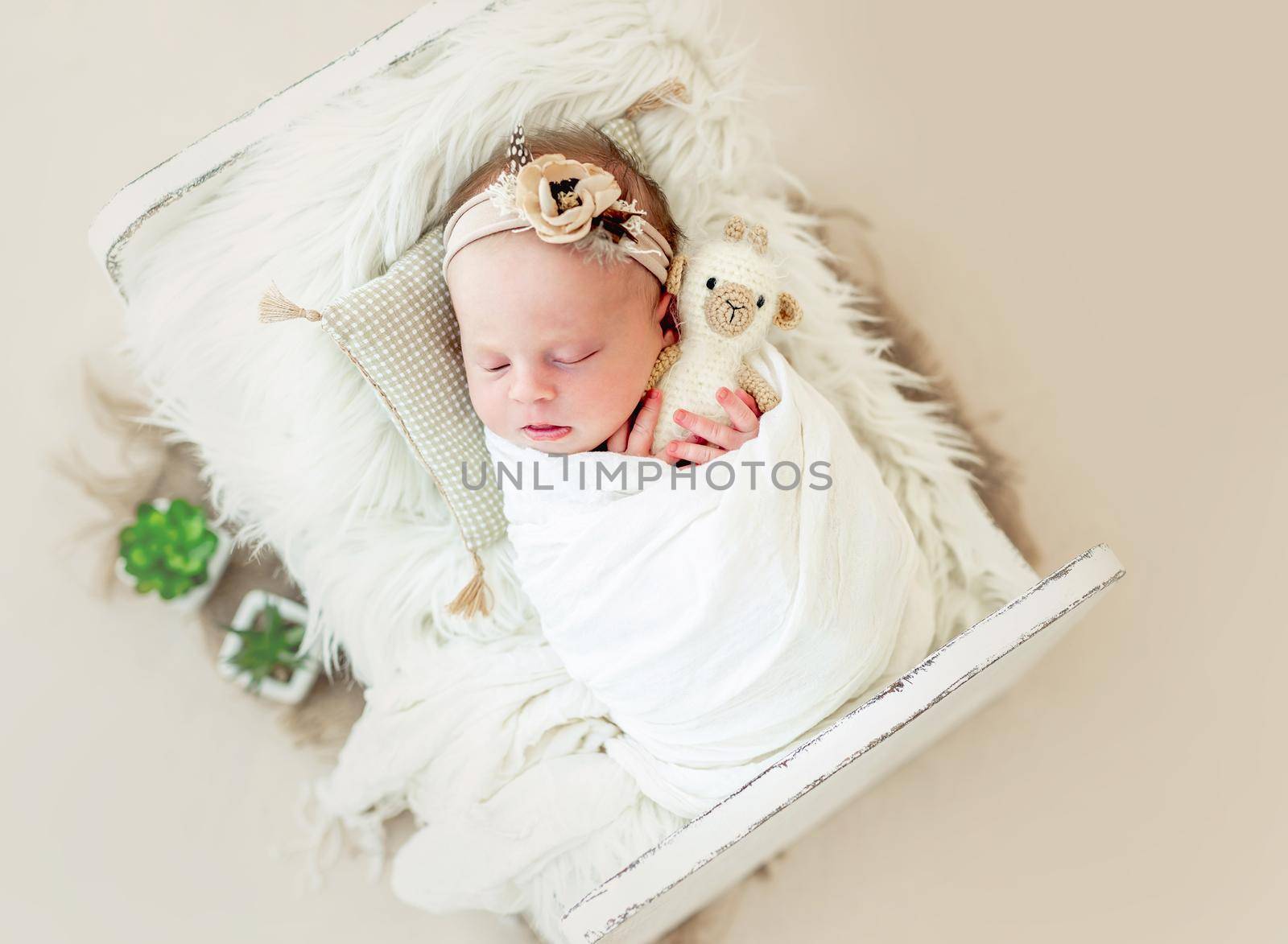 Sleeping newborn baby girl wrapped in white blanket in a small crib