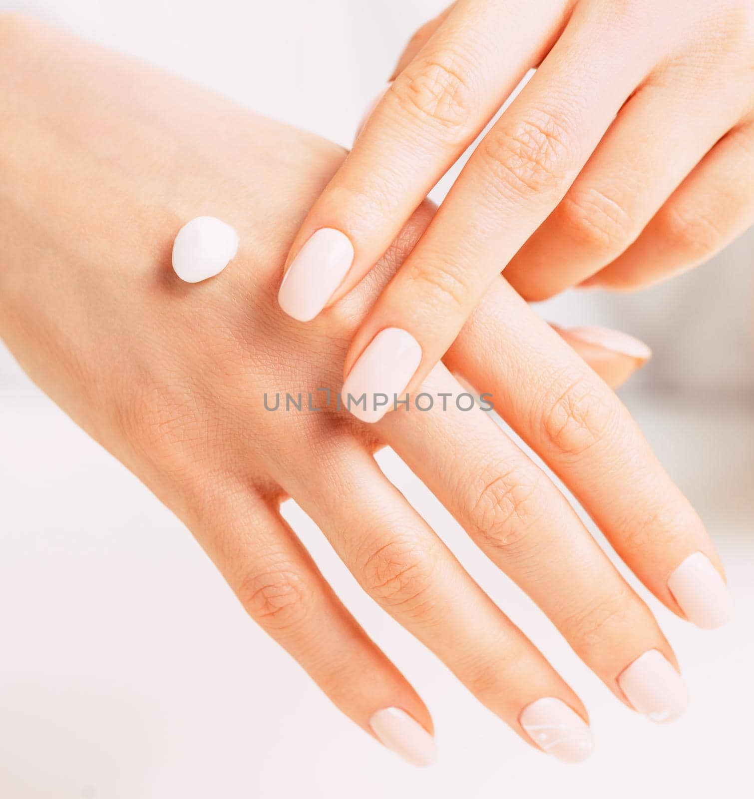 Young female hands with manicure of beige natural color applying moisturizing cream, concept of skincare and beauty.