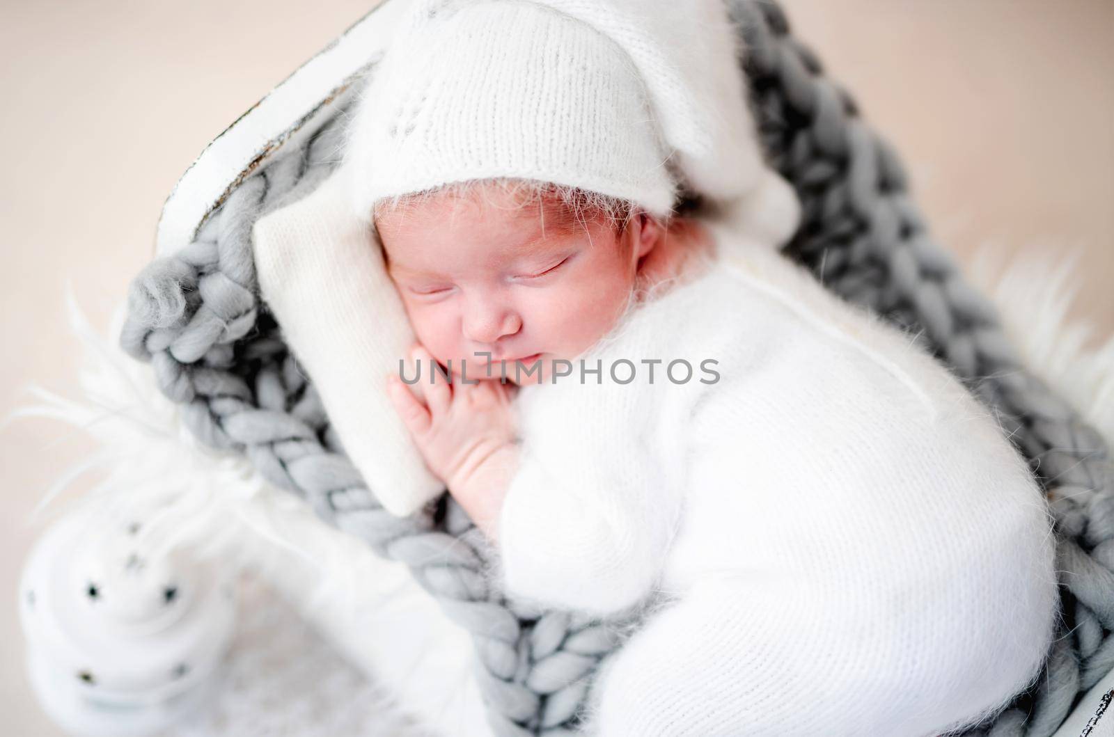 Cute newborn in white suit and hat sleeping on tiny bed