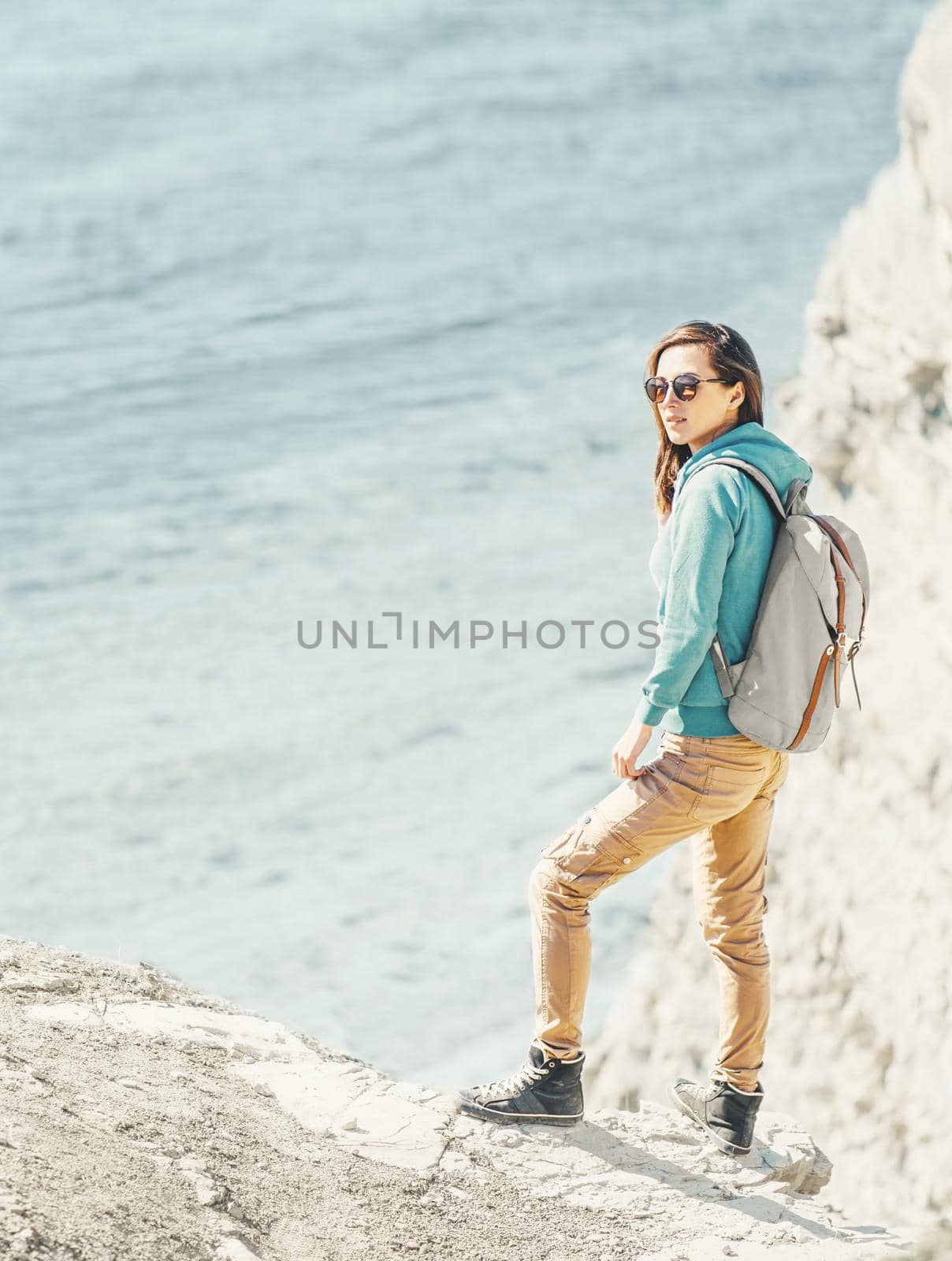 Traveler girl with backpack walking on high coast on background of sea in summer.
