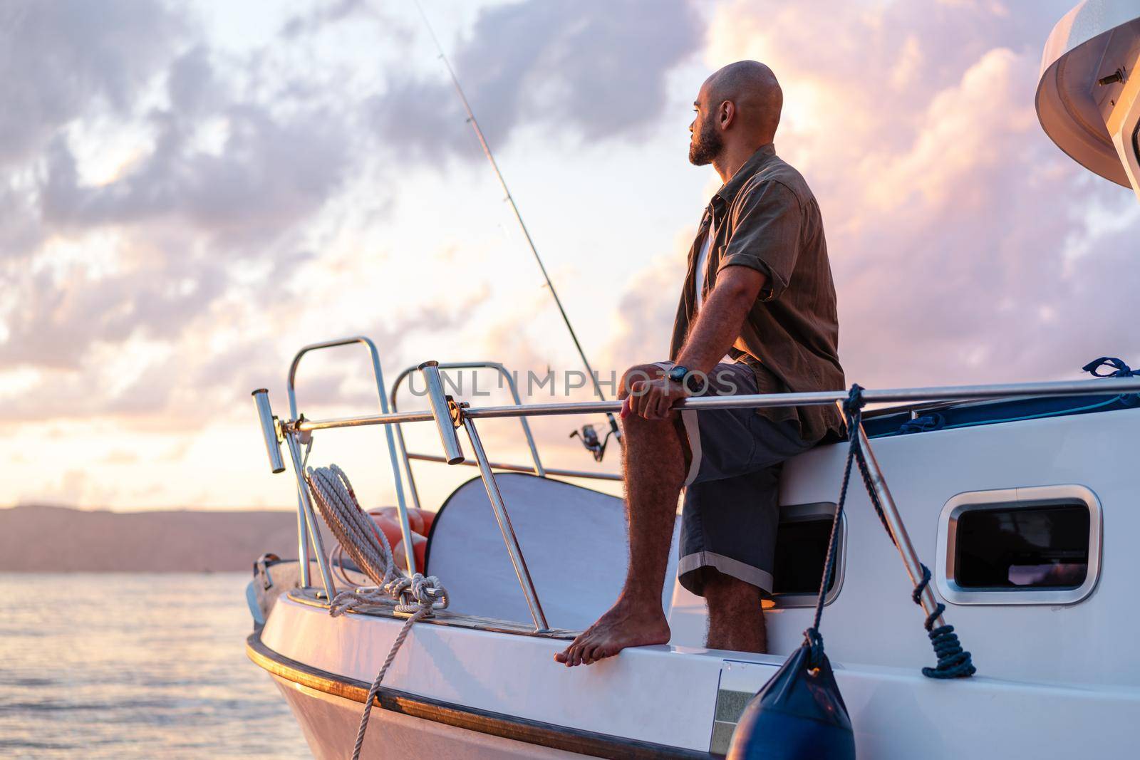 Young african american man standing with fishing rod on a sailboat fishing in open sea on sunset, close up