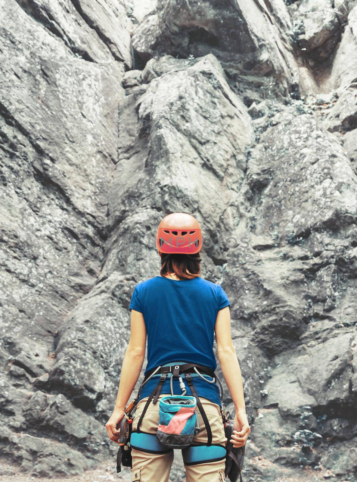 Unrecognizable young woman wearing in climbing equipment standing in front of a rock outdoor and preparing to free climb, rear view.