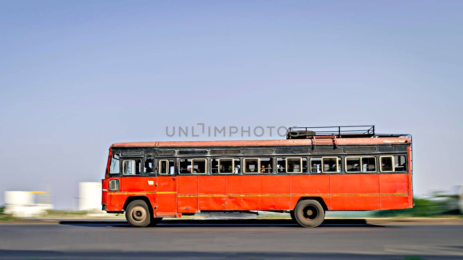 Background blur, pan image of non air-conditioned red intercity bus in Maharashtra, speeding on the street. by lalam