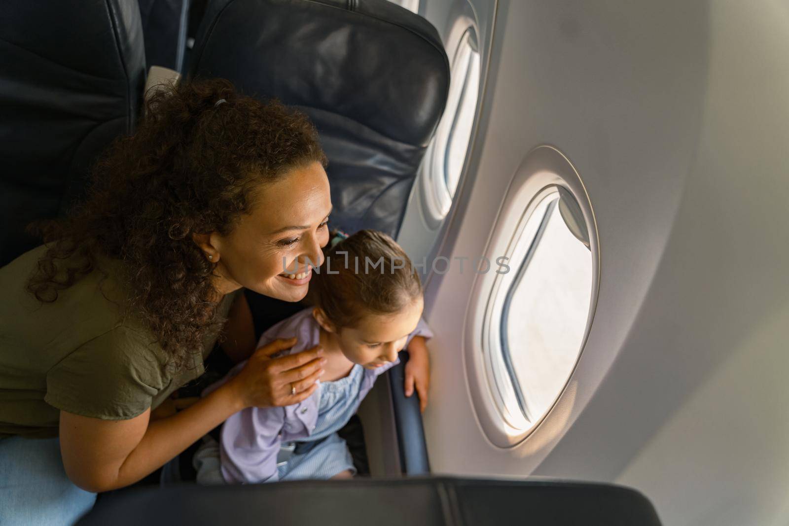 Smiling mom and her kid looking at the scenery outside the plane window by Yaroslav_astakhov