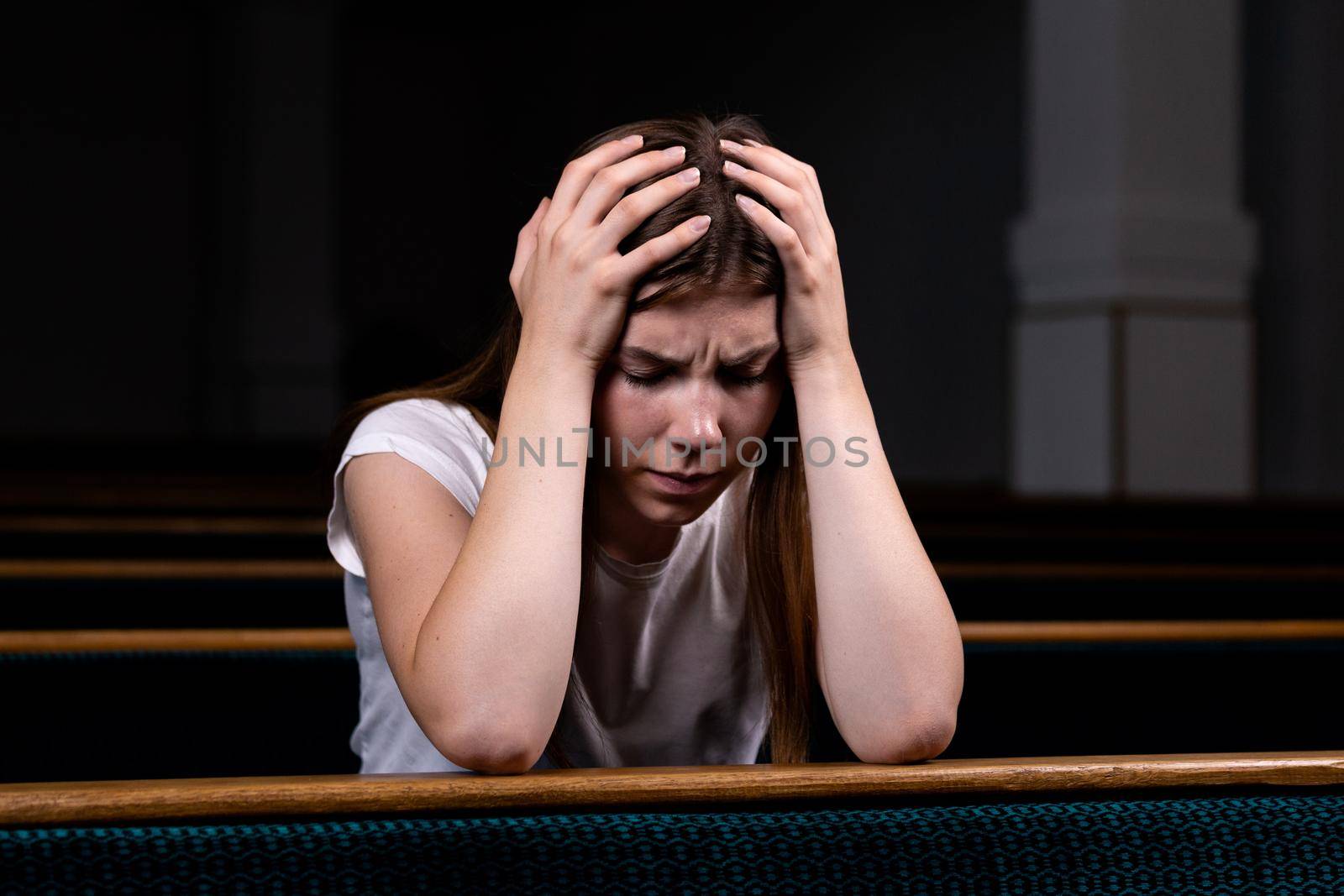 A Sad Christian girl in white shirt is sitting and praying with humble heart in the church by lunarts
