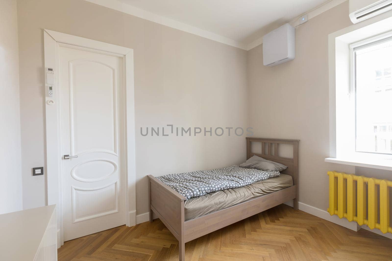 Minimalist style interior design of modern light bedroom with wooden single bed placed in corner between door and window with yellow radiator