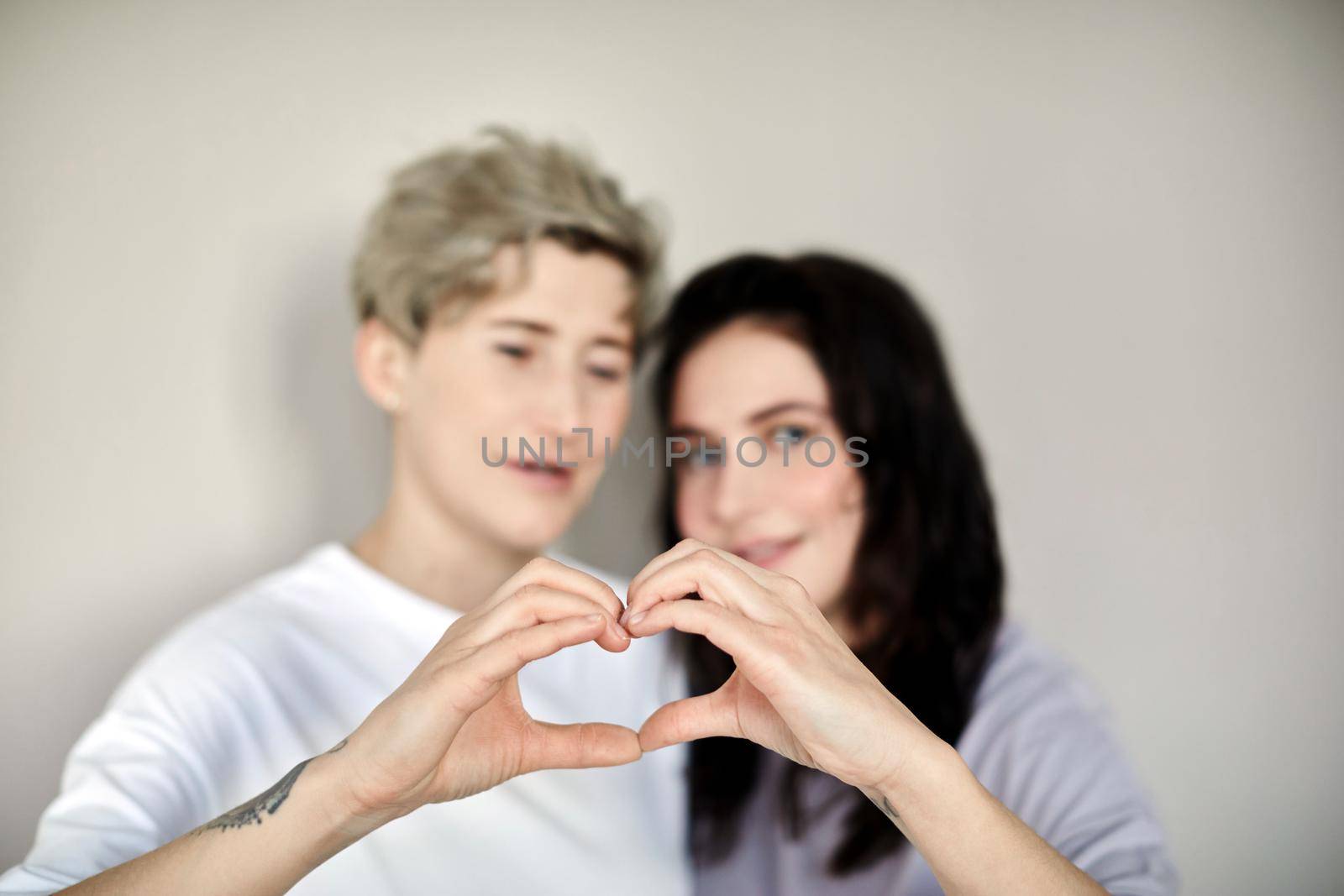 Selective focus of heart made by same sex female partners standing close and showing love gesture