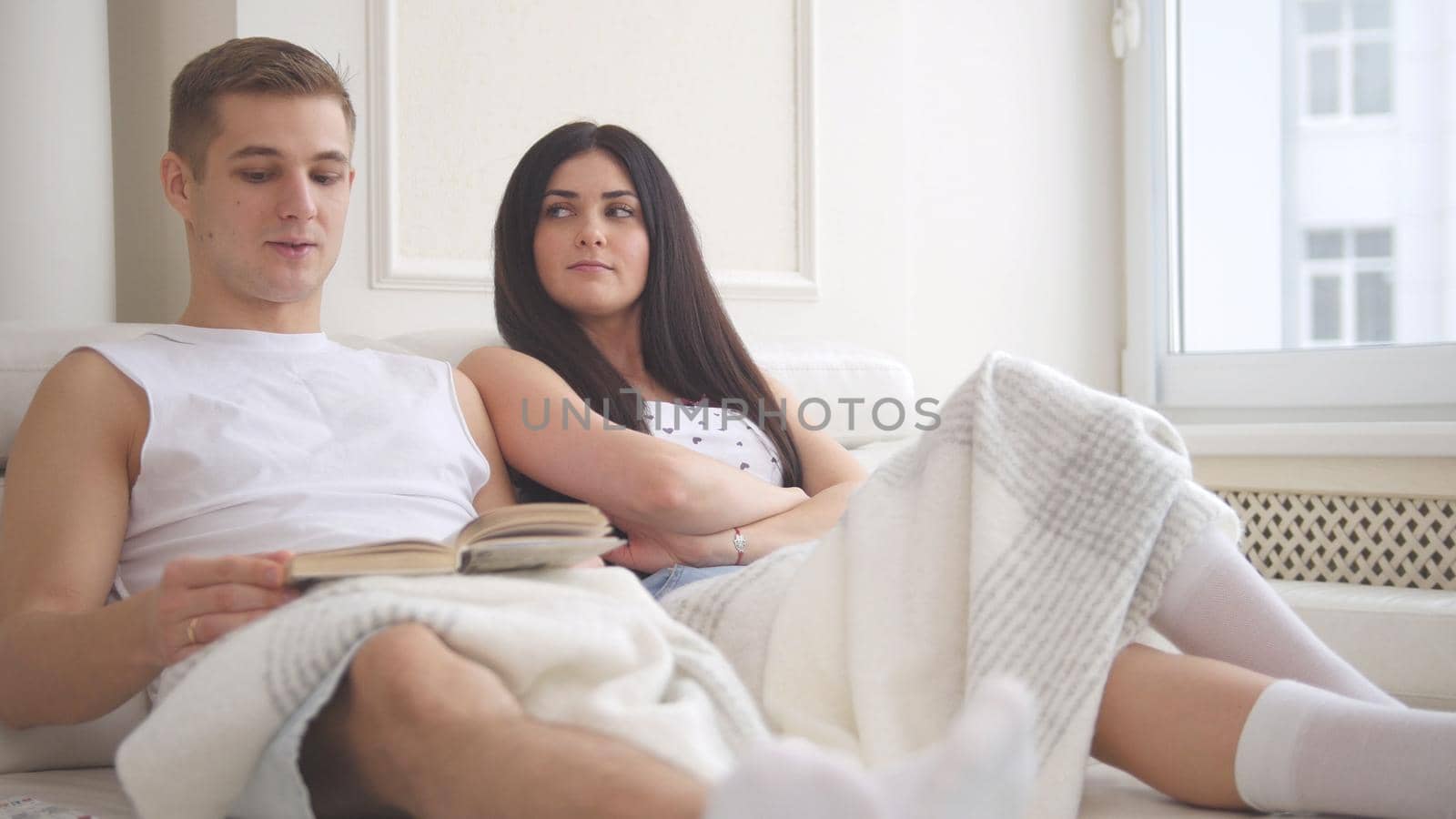 Happy young attractive couple sitting together on the couch talking, laughing and reading a book, people's attitudes