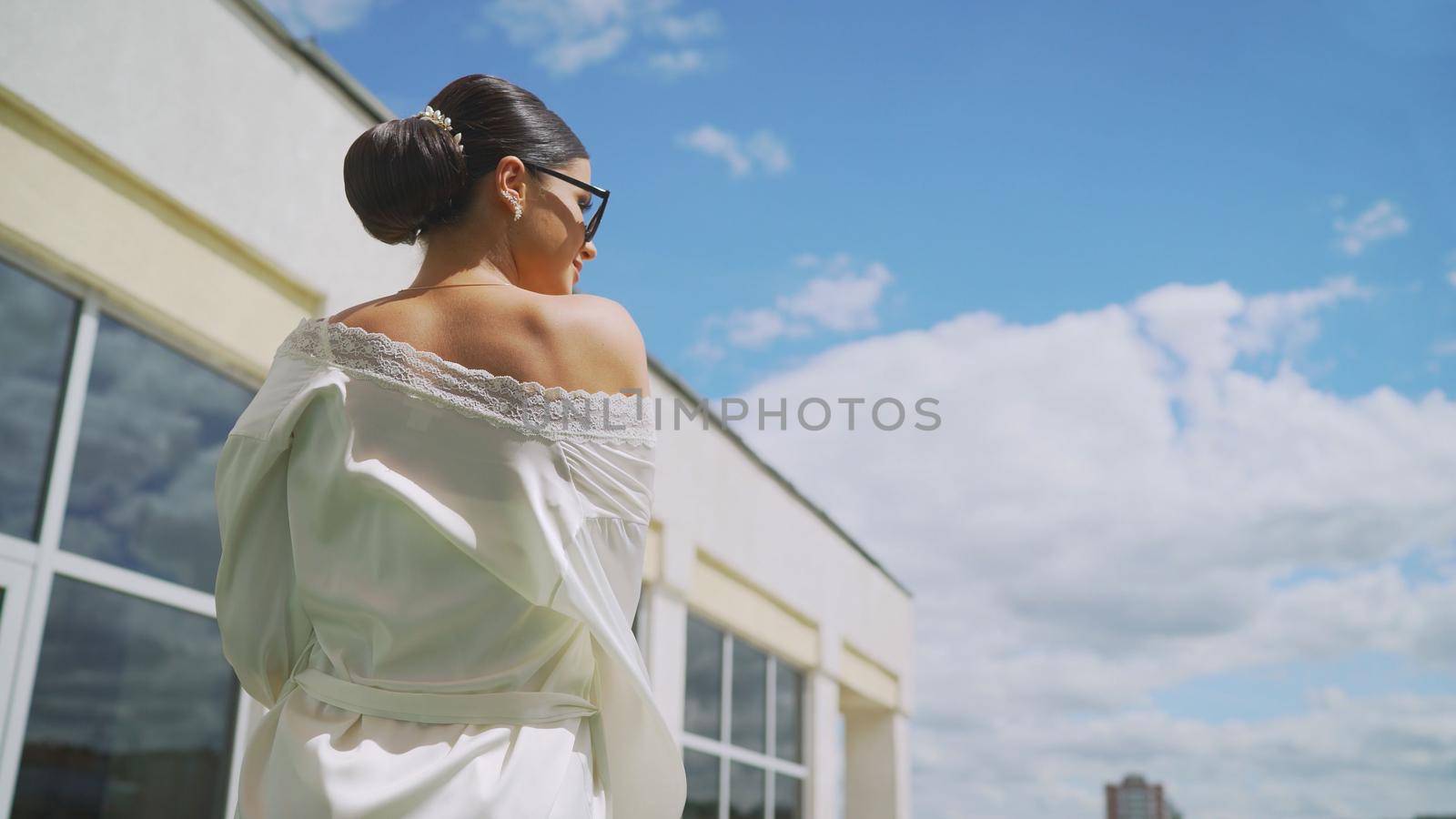 Stylish girl in a white robe on the roof of the hotel. Girl in sunglasses and a white robe. Cute laughing blogger girl in a white coat. Portrait of a sexy charming woman in a robe and sunglasses. Vacation concept.