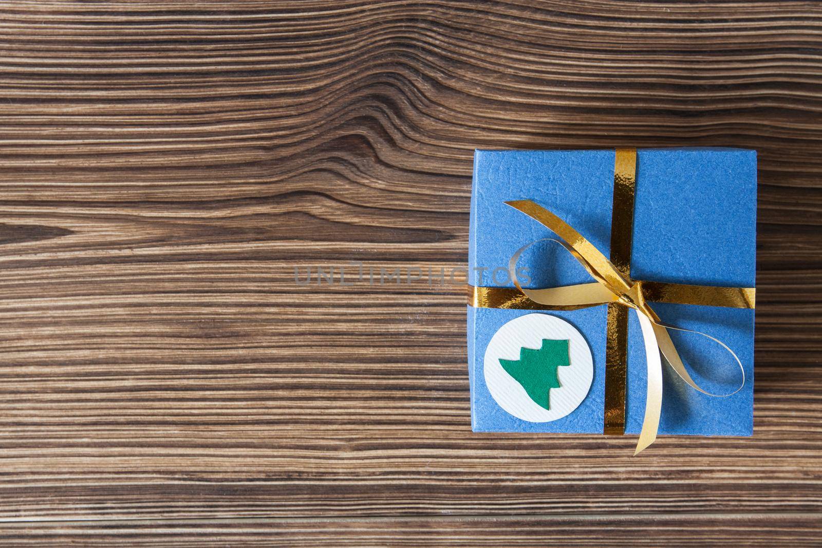 Blue gift box with golden ribbon on a brown wooden background for Christmas and New Year