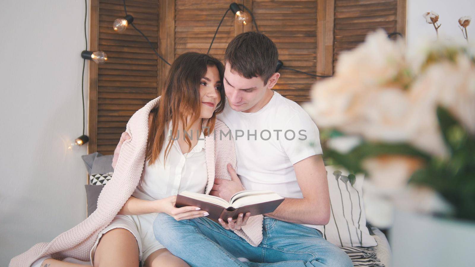 Young man and woman relaxing at home - reading the book on sofa kissing each other happy by Studia72